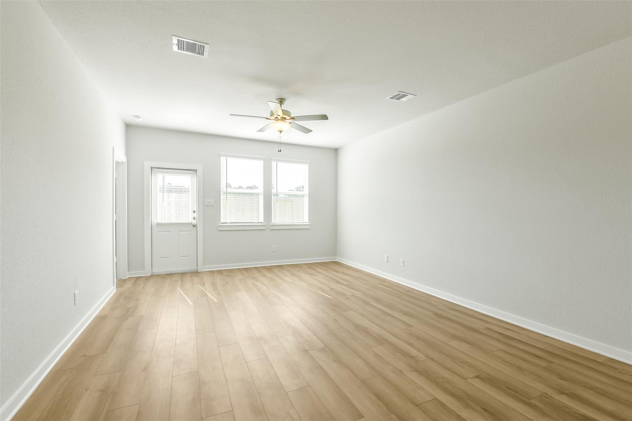 Spacious empty upstairs room with light hardwood floors, white walls, ceiling fan, and large windows in Davidson Homes San Marcos E, Cleveland, Texas