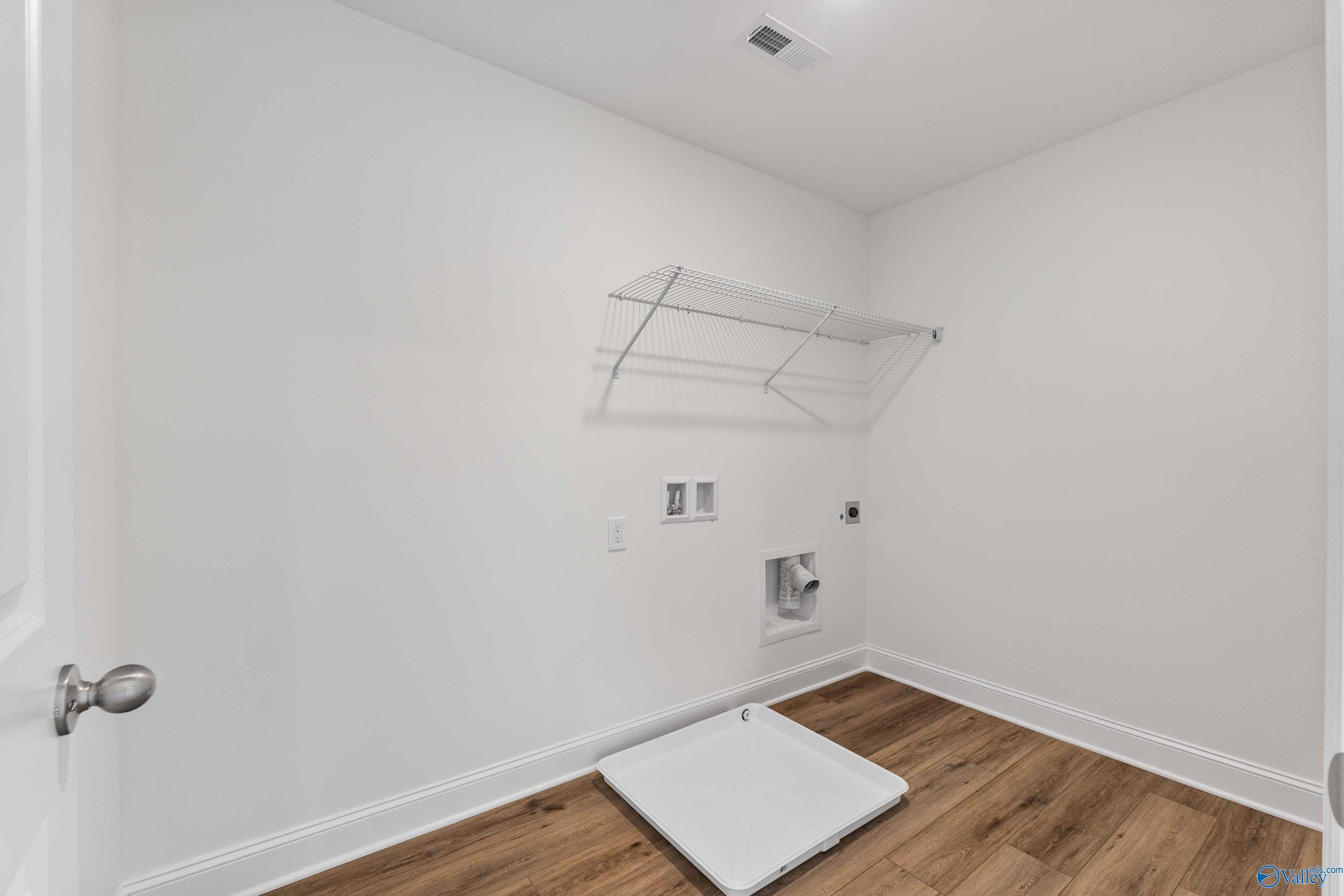 Modern laundry room with open wire shelving, washer-dryer hookups, and laminate wood floors in Davidson Homes Shelby A, New Market, AL