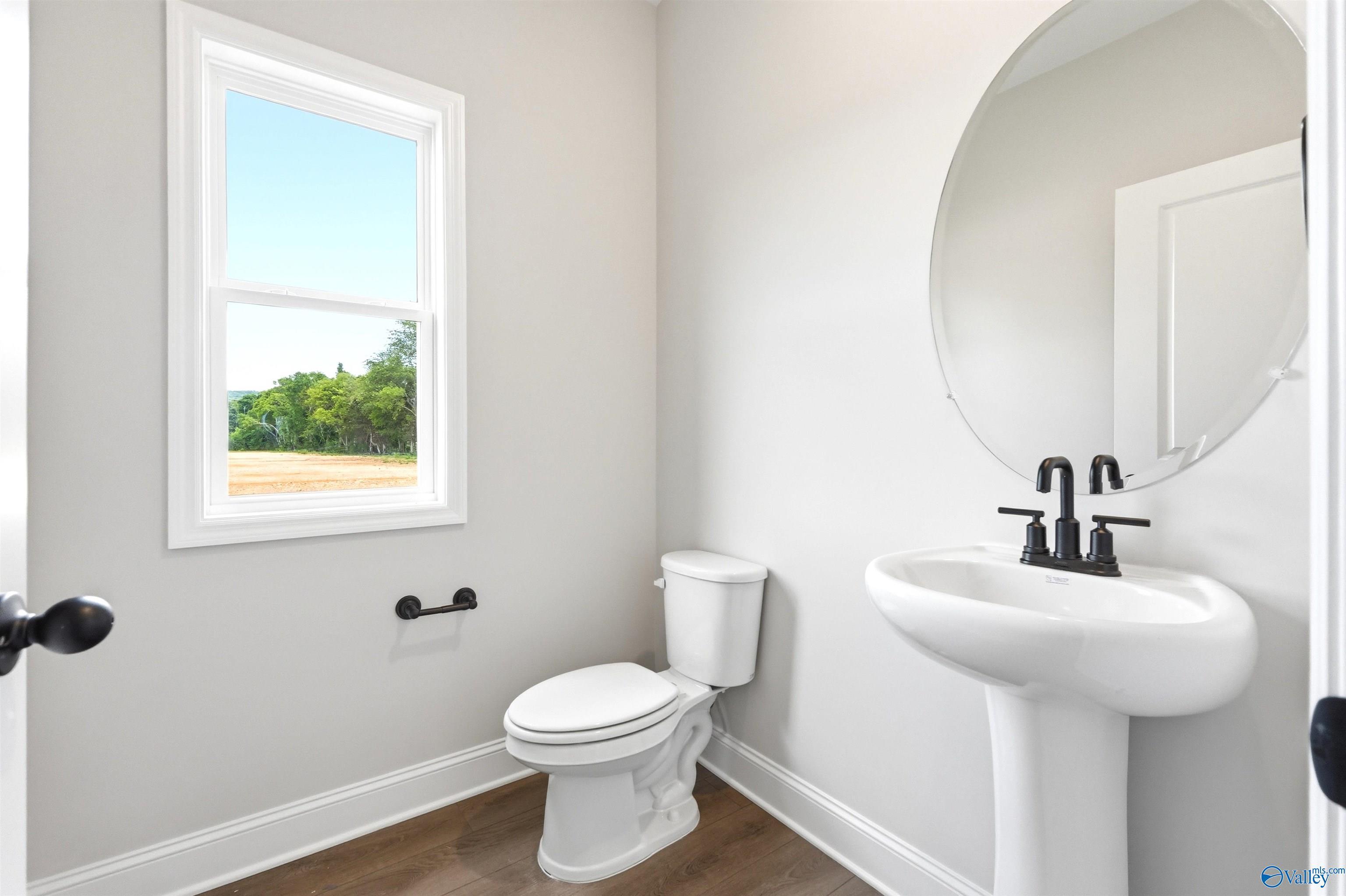 Modern half-bath with pedestal sink and round mirror in The Chelsea D floor plan at Berry Cove, New Market, Alabama.