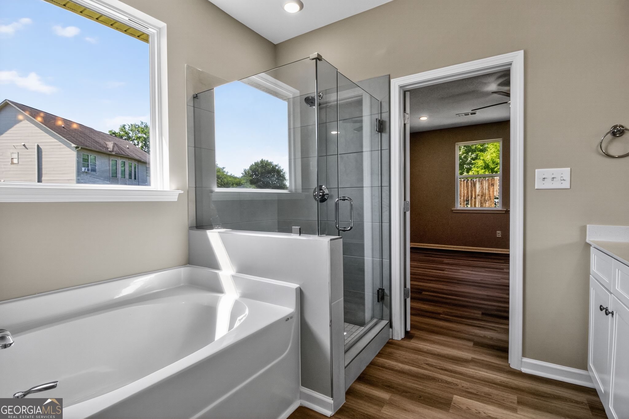 Modern master bathroom featuring glass shower, deep soaking tub, and sunny window in Evermore Homes The Luna, Perry, Georgia