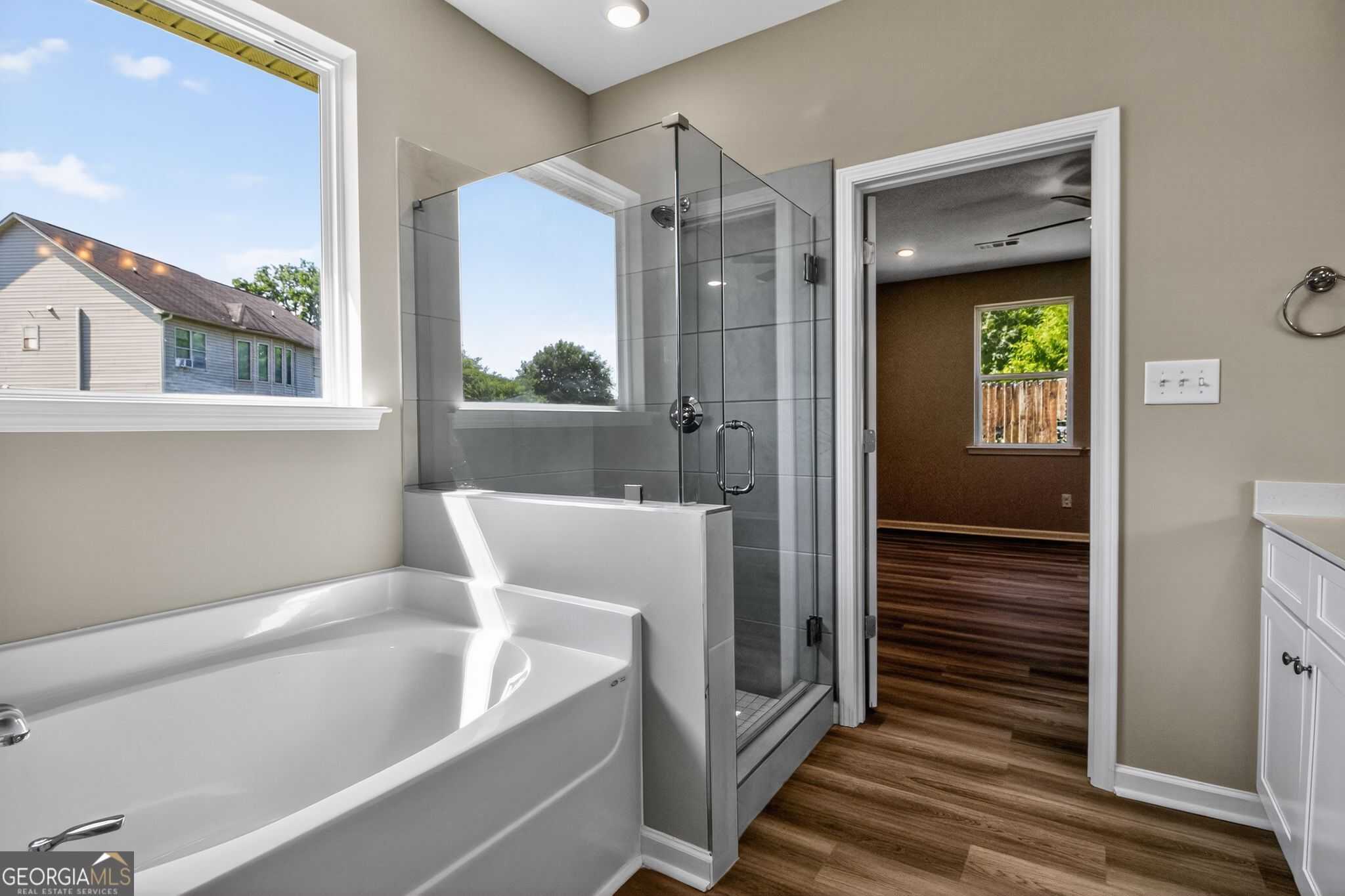 Modern master bathroom featuring glass shower, deep soaking tub, and sunny window in Evermore Homes The Luna, Perry, Georgia