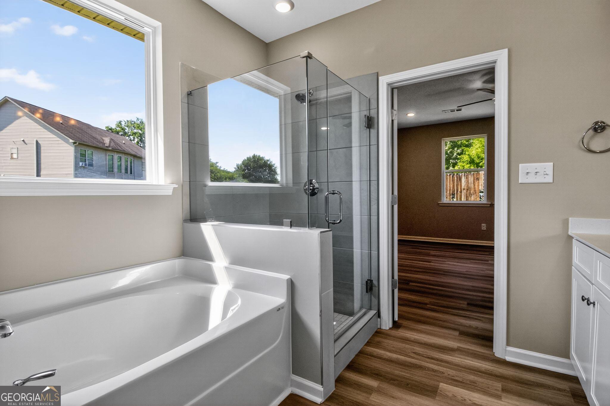 Modern master bathroom featuring glass shower, deep soaking tub, and sunny window in Evermore Homes The Luna, Perry, Georgia