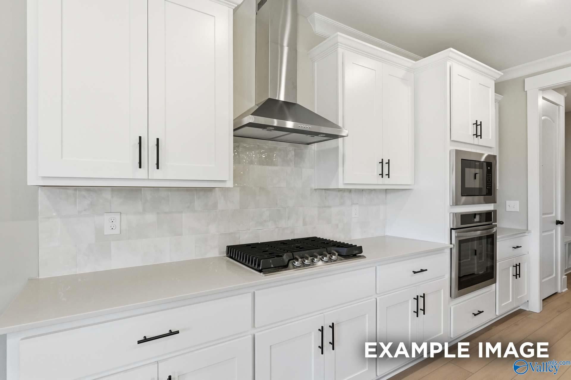 Modern white shaker kitchen with quartz counters, gas cooktop, stainless hood and subway tile in The Emory 4-bedroom home, Decatur AL