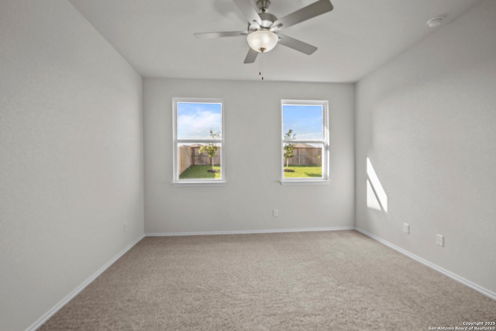 Bright secondary bedroom with ceiling fan, large windows to lush backyard, carpeted floor in Davidson Homes The Asheville J, San Antonio