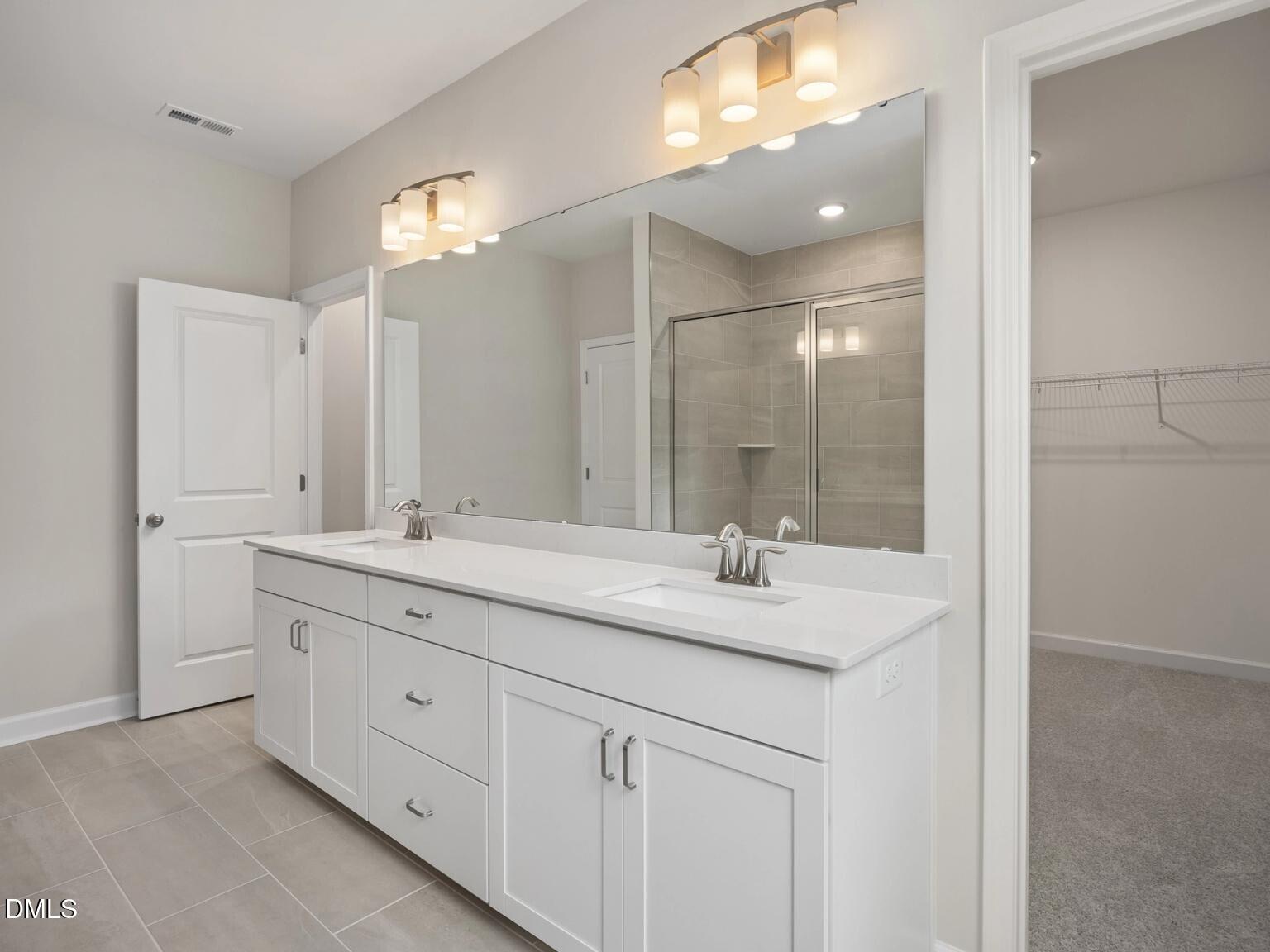 Modern master bathroom featuring white double vanity, frameless mirrors, glass shower, and neutral tile in Davidson Homes The Beech B, Wake Forest, NC
