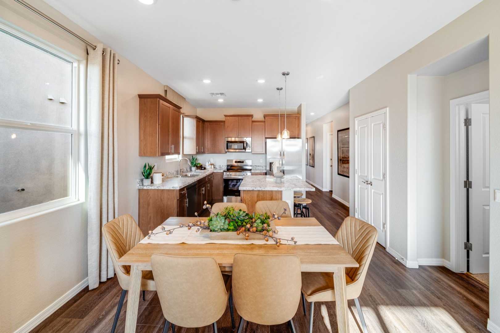Bright open-concept kitchen and dining in The Savannah C, featuring oak cabinets, large island, wooden table with beige chairs, and sunlit windows