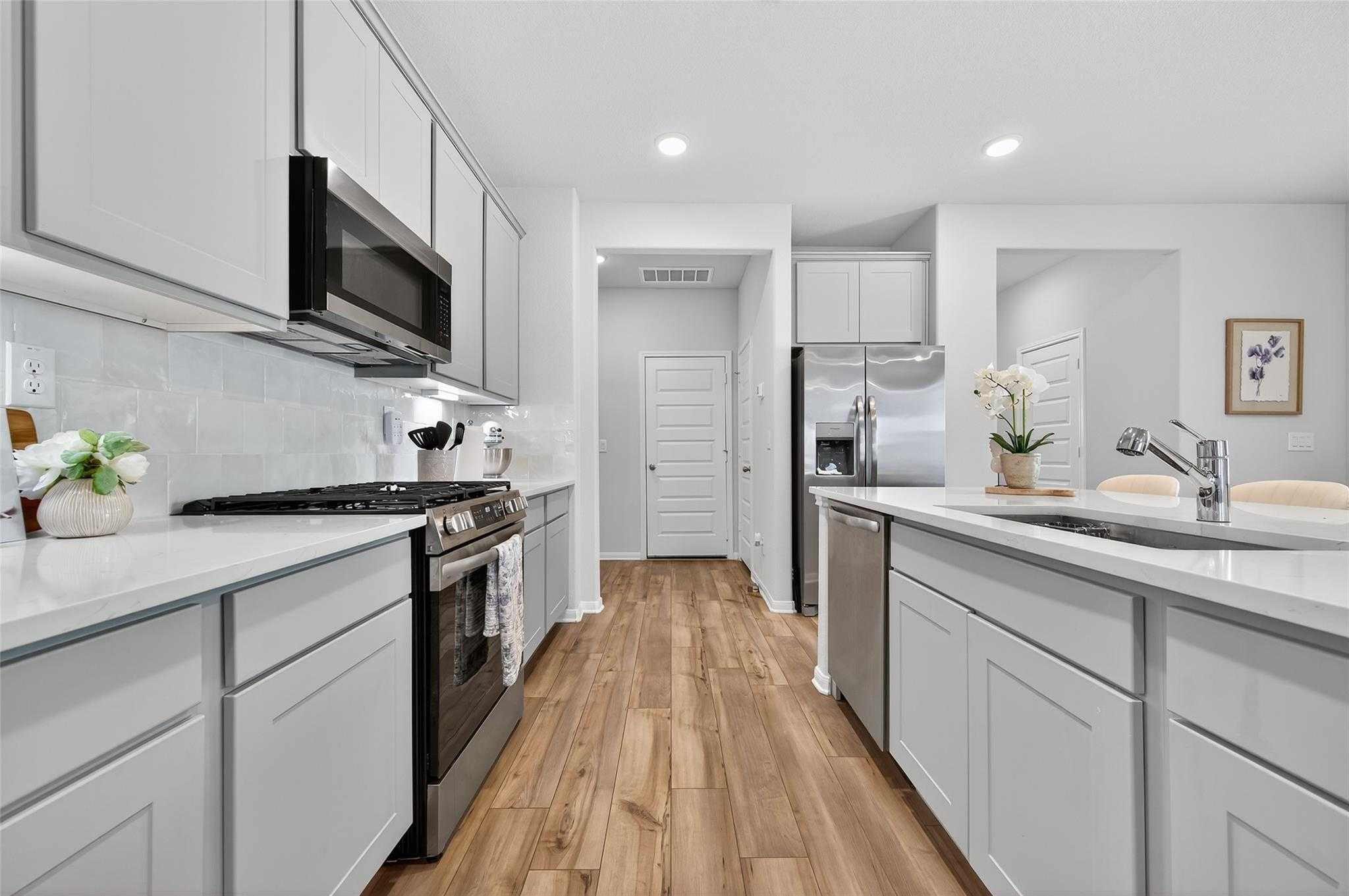 Modern white shaker kitchen with stainless steel appliances, quartz counters, subway tile in Davidson Homes The Brazos E, Magnolia TX