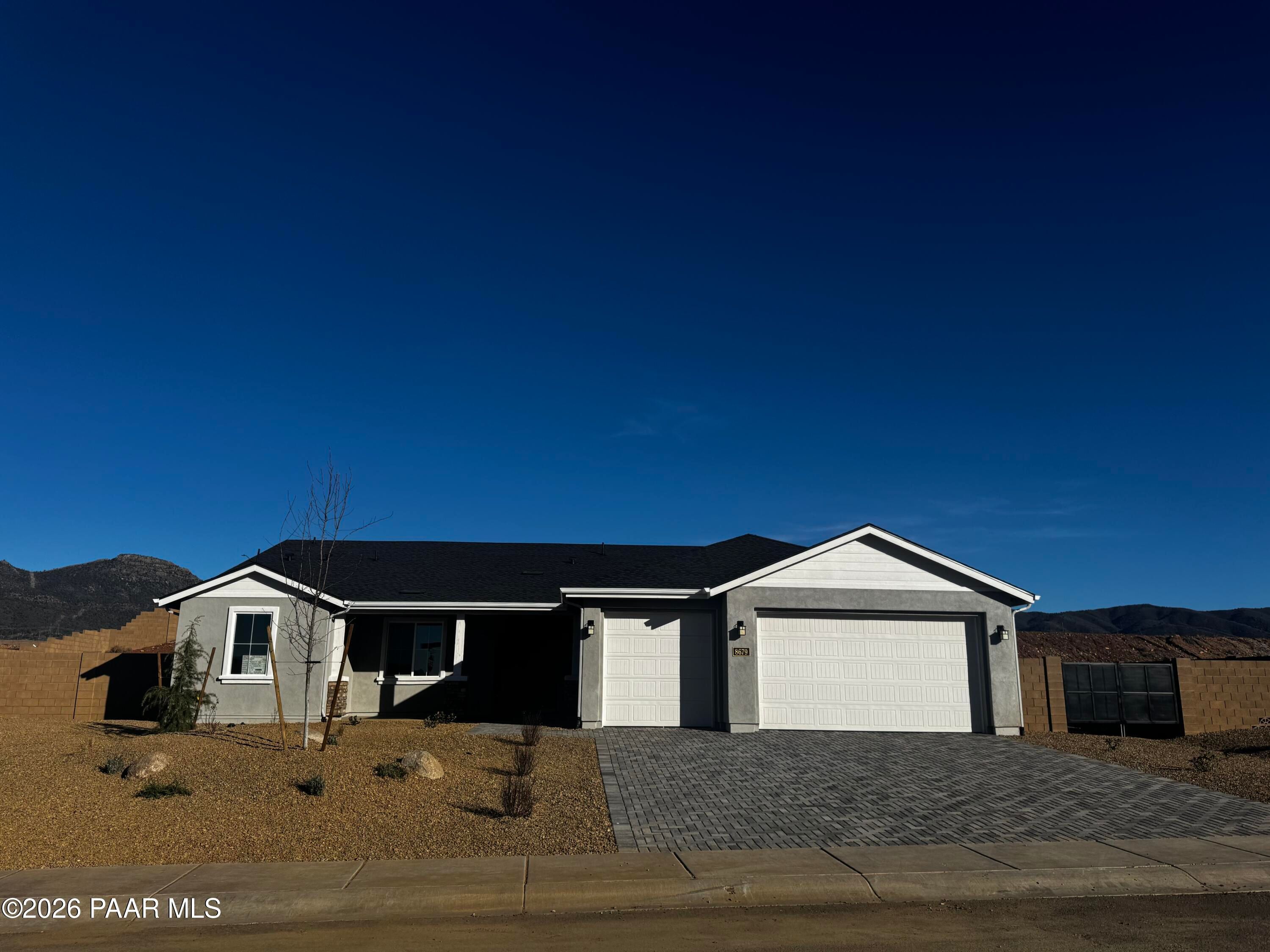 Modern single-story home with 3-car garage, white stucco exterior, paver driveway, desert landscaping, and mountain backdrop in Prescott Valley, Arizona