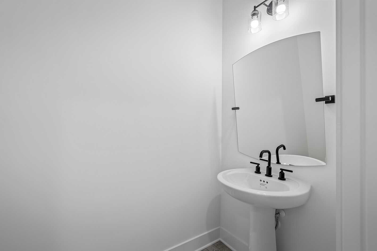 Modern powder room with white pedestal sink, black faucet, curved mirror, and sconce lights in Davidson Homes The Alston A, Murfreesboro, TN