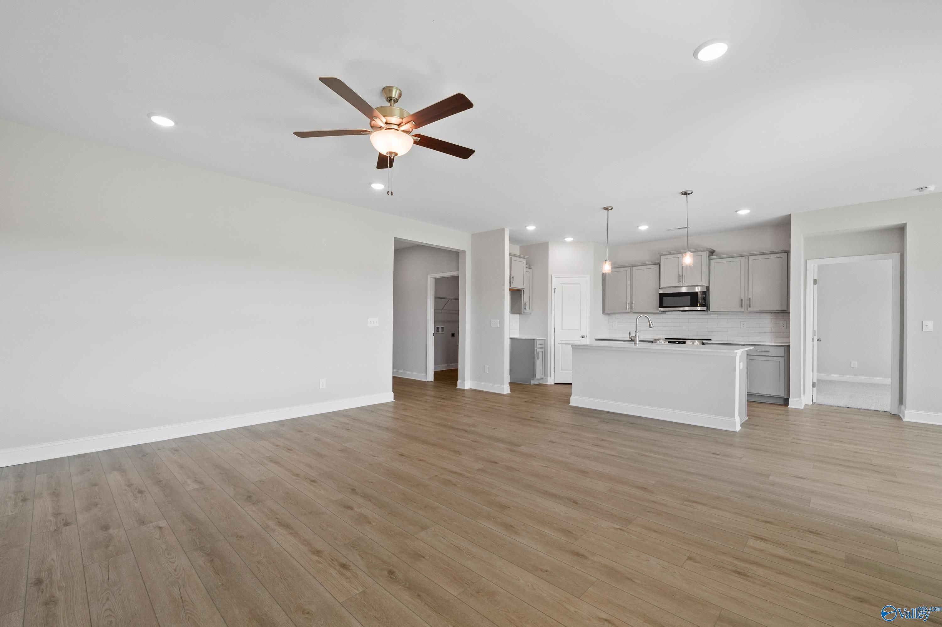 Open-concept kitchen and living area with white cabinets, island sink, hardwood floors, and ceiling fan in Davidson Homes The Everett, Hazel Green, Alabama