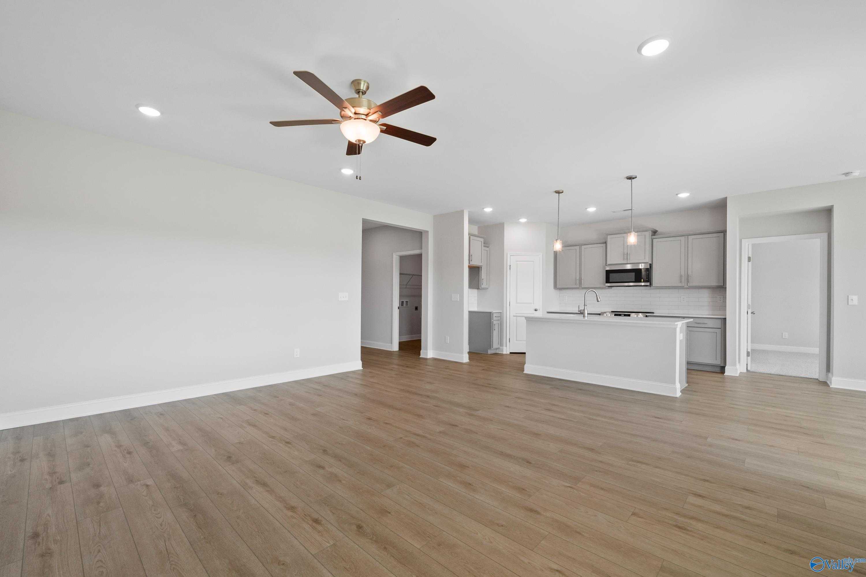 Open-concept kitchen and living area with white cabinets, island sink, hardwood floors, and ceiling fan in Davidson Homes The Everett, Hazel Green, Alabama