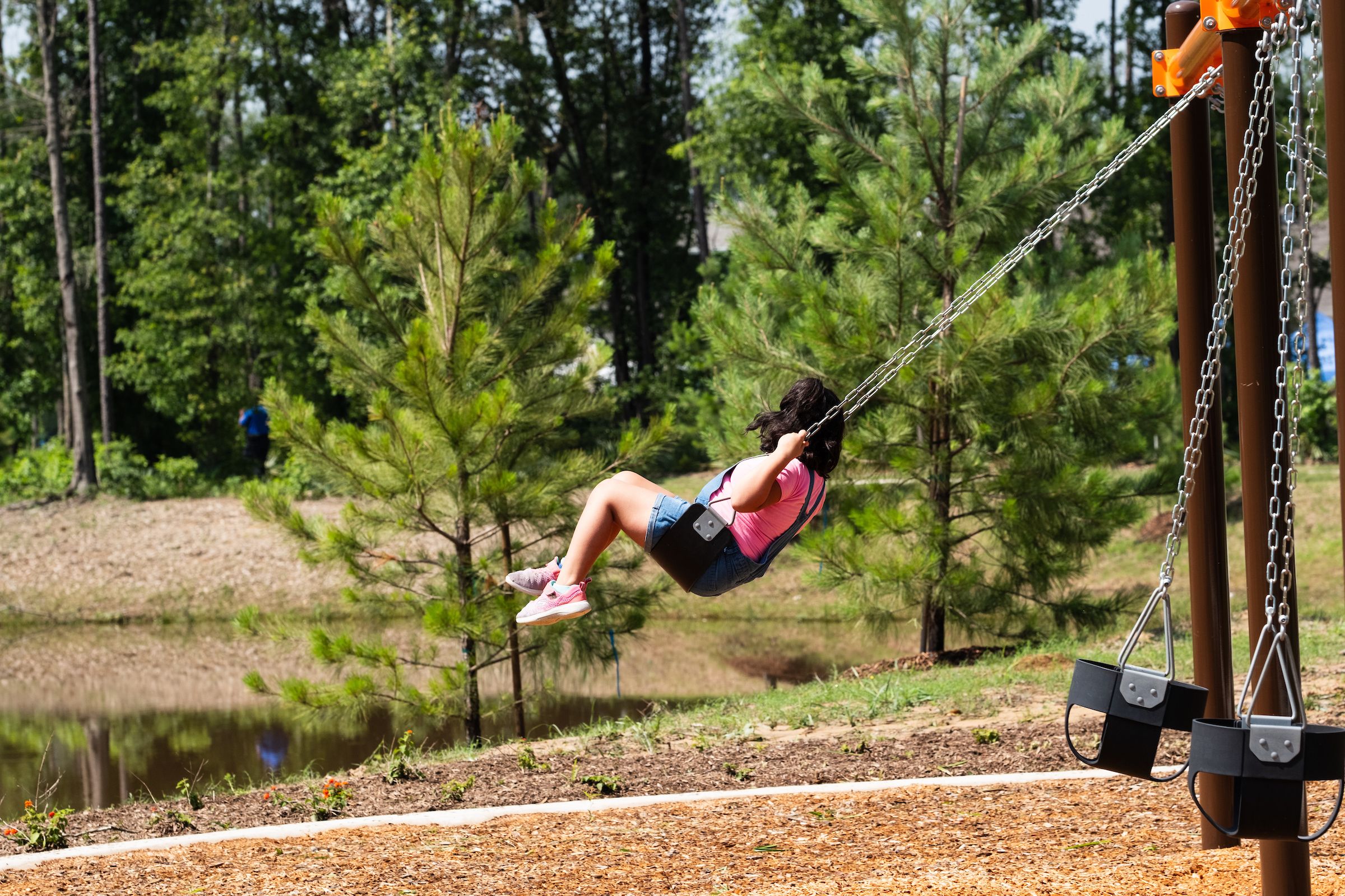 Child swinging on playground set at Robins Landing in Houston Texas amid pine trees and scenic pond