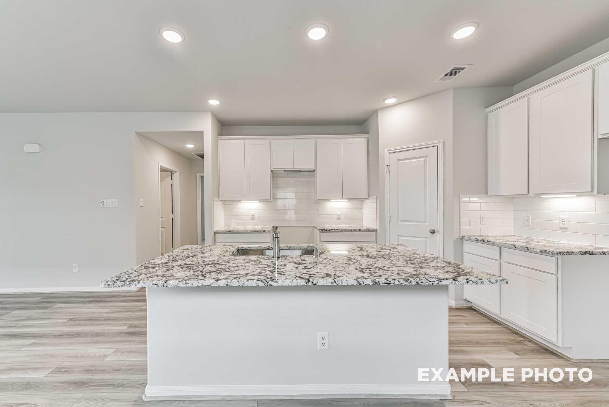 Modern white cabinet kitchen with granite island sink and recessed lights in Davidson Homes Riviera A, Rosharon TX