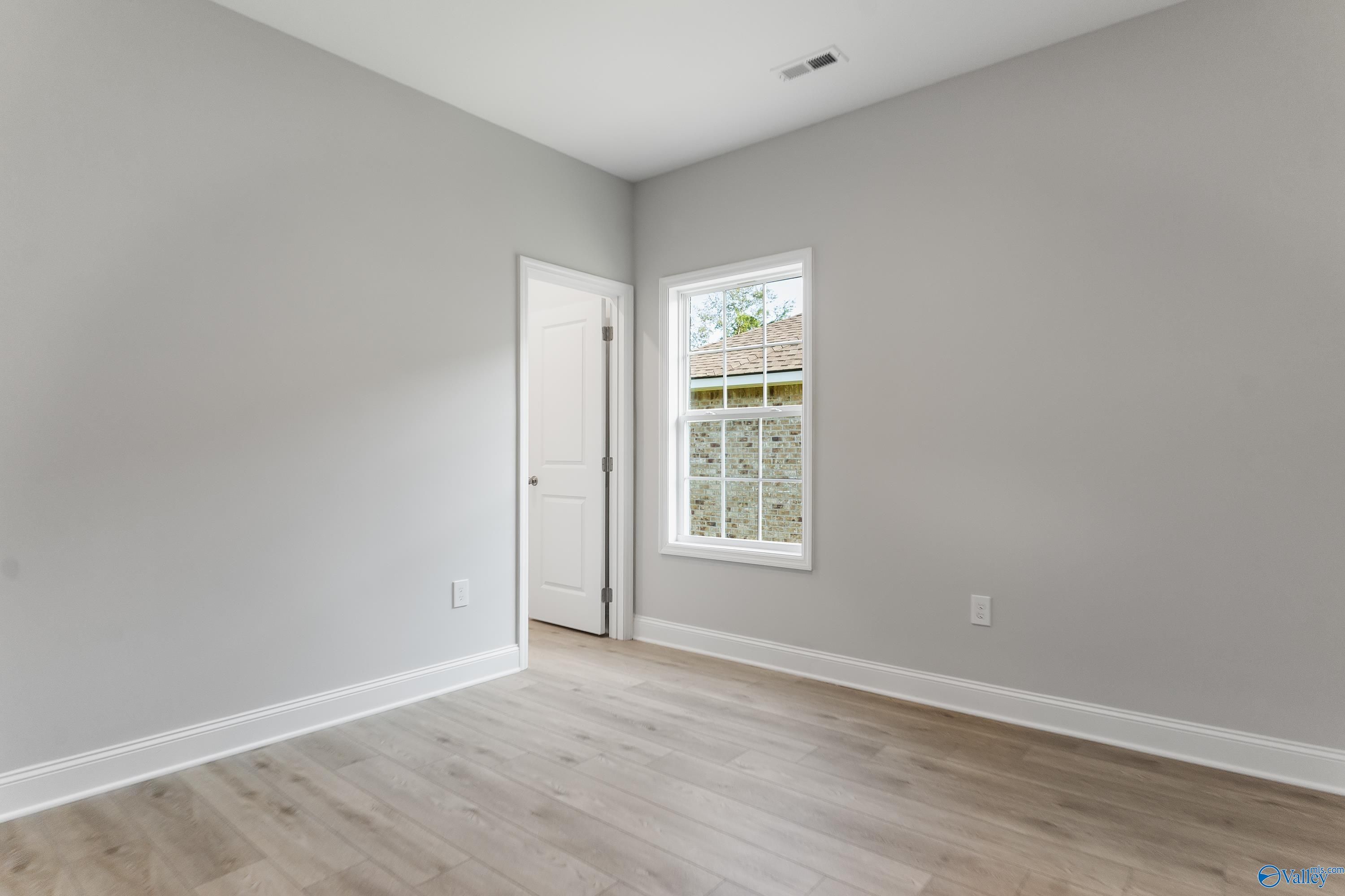 Bright secondary bedroom with light gray walls, hardwood floors, and window view in Davidson Homes The Daphne C, Huntsville Alabama