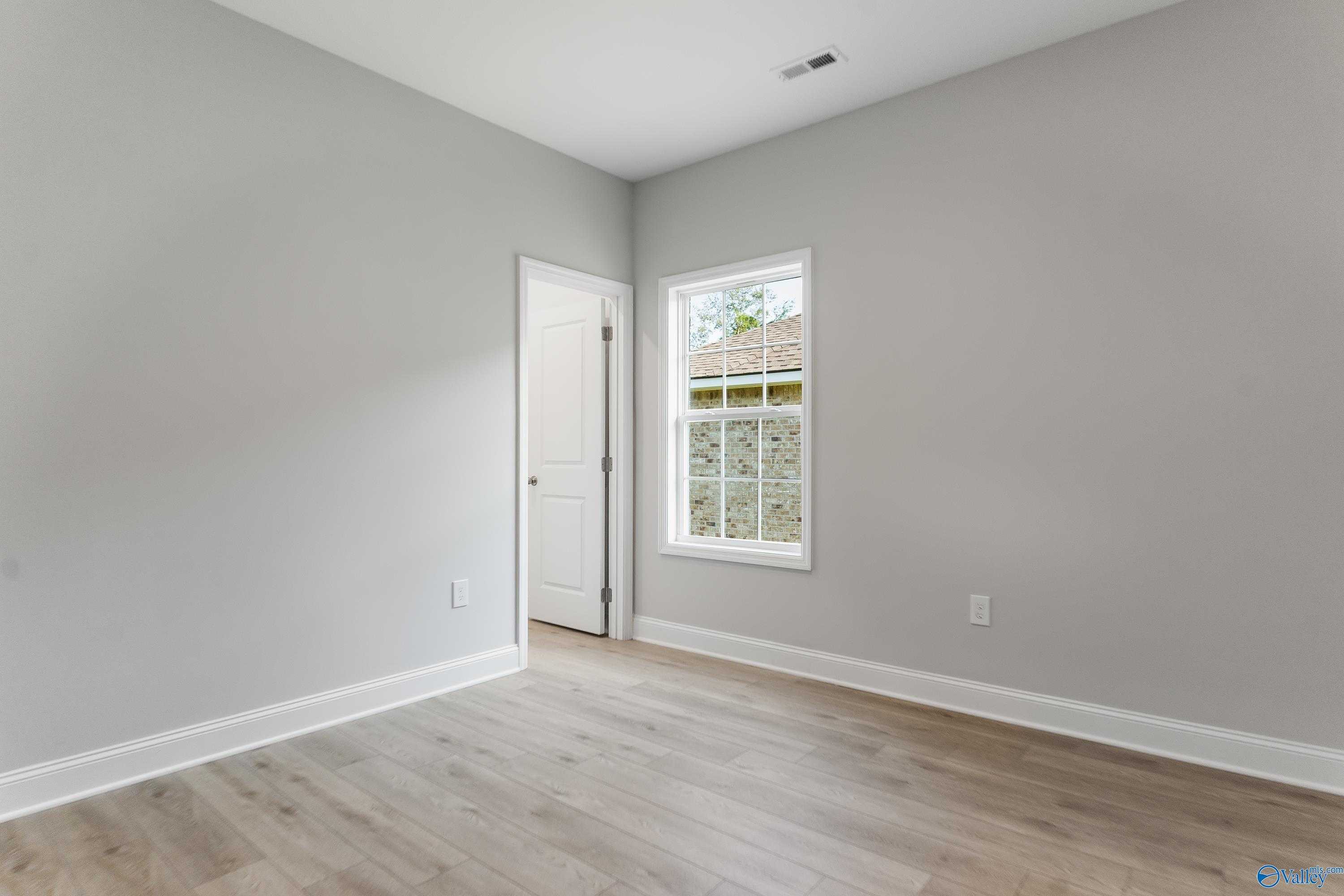 Spacious empty bedroom with light gray walls, luxury vinyl plank floors, white door, and large window in Davidson Homes The Daphne C, Huntsville AL