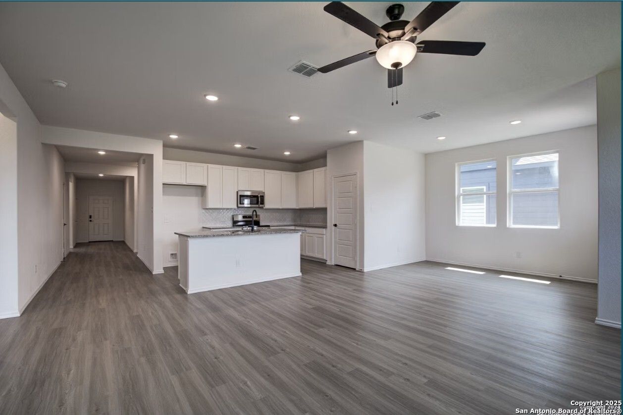 Open-concept kitchen and living area with white cabinets, stainless appliances, island, and ceiling fans in The Daphne H by Davidson Homes, Seguin, TX