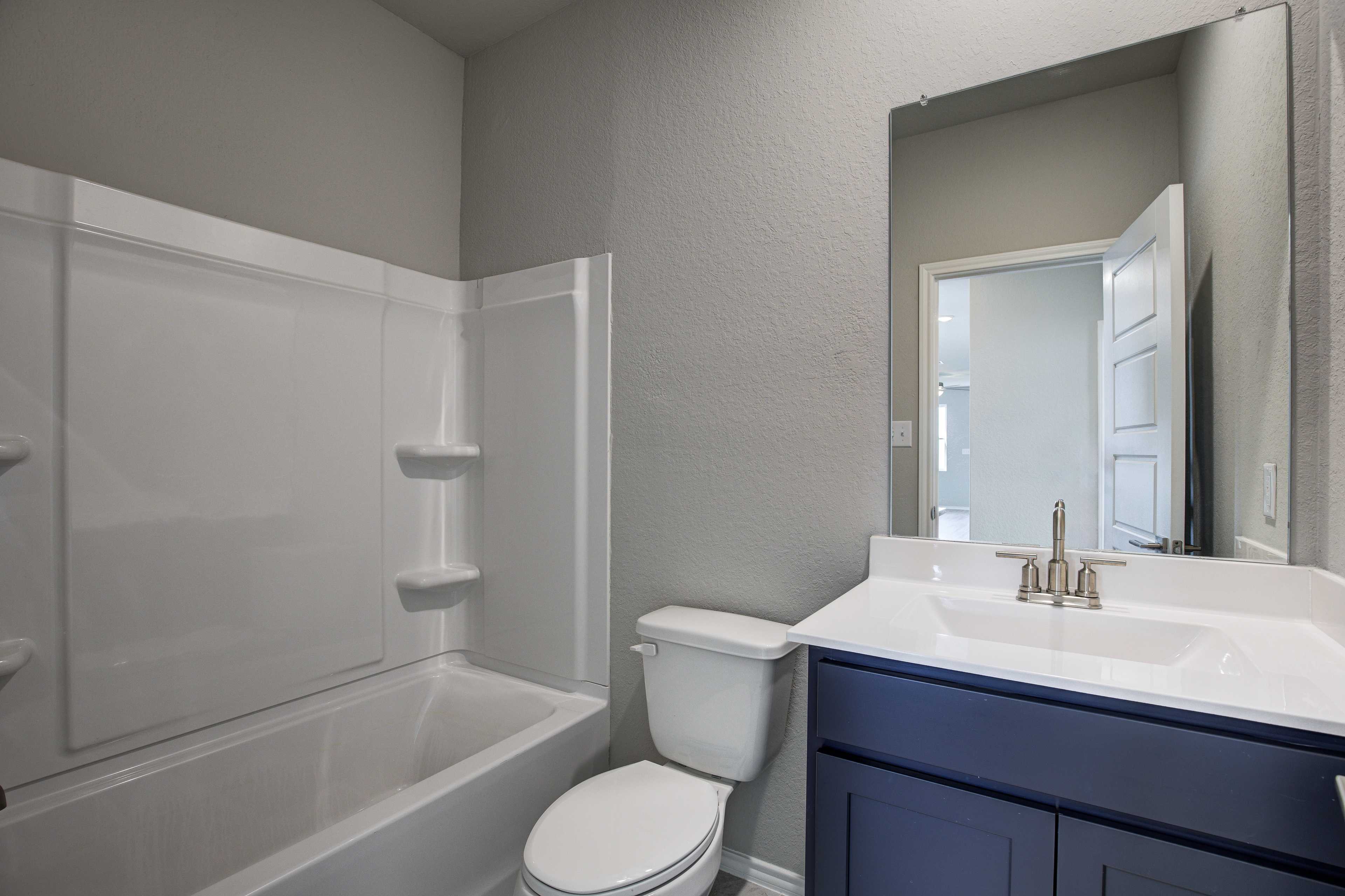 Master bathroom in The Frio B by Davidson Homes with white tub, walk-in shower, navy vanity, toilet, and gray walls