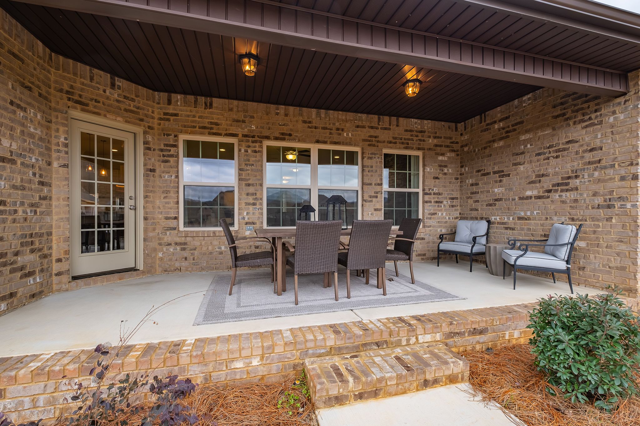 Covered patio with brick exterior, dining table, lounge chairs, and potted plants at Chimney Creek in Hampton Cove, Alabama