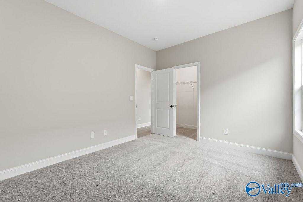 Spacious master bedroom with walk-in closet, large window, and neutral walls in Davidson Homes The Rockford B, Hartselle, Alabama