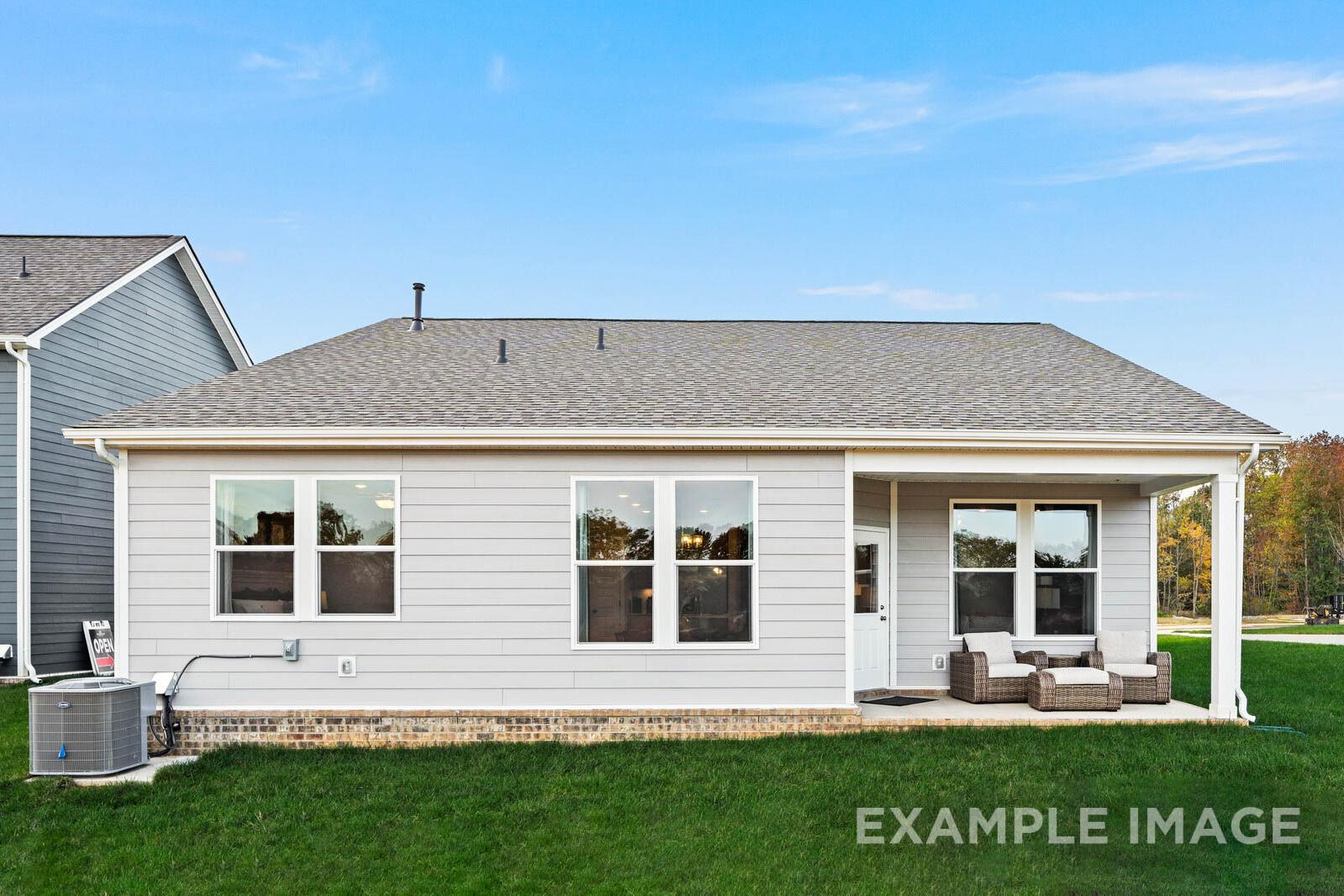 Rear view of The Franklin B single-story home featuring gray siding, covered porch with wicker seating, large windows, and green lawn