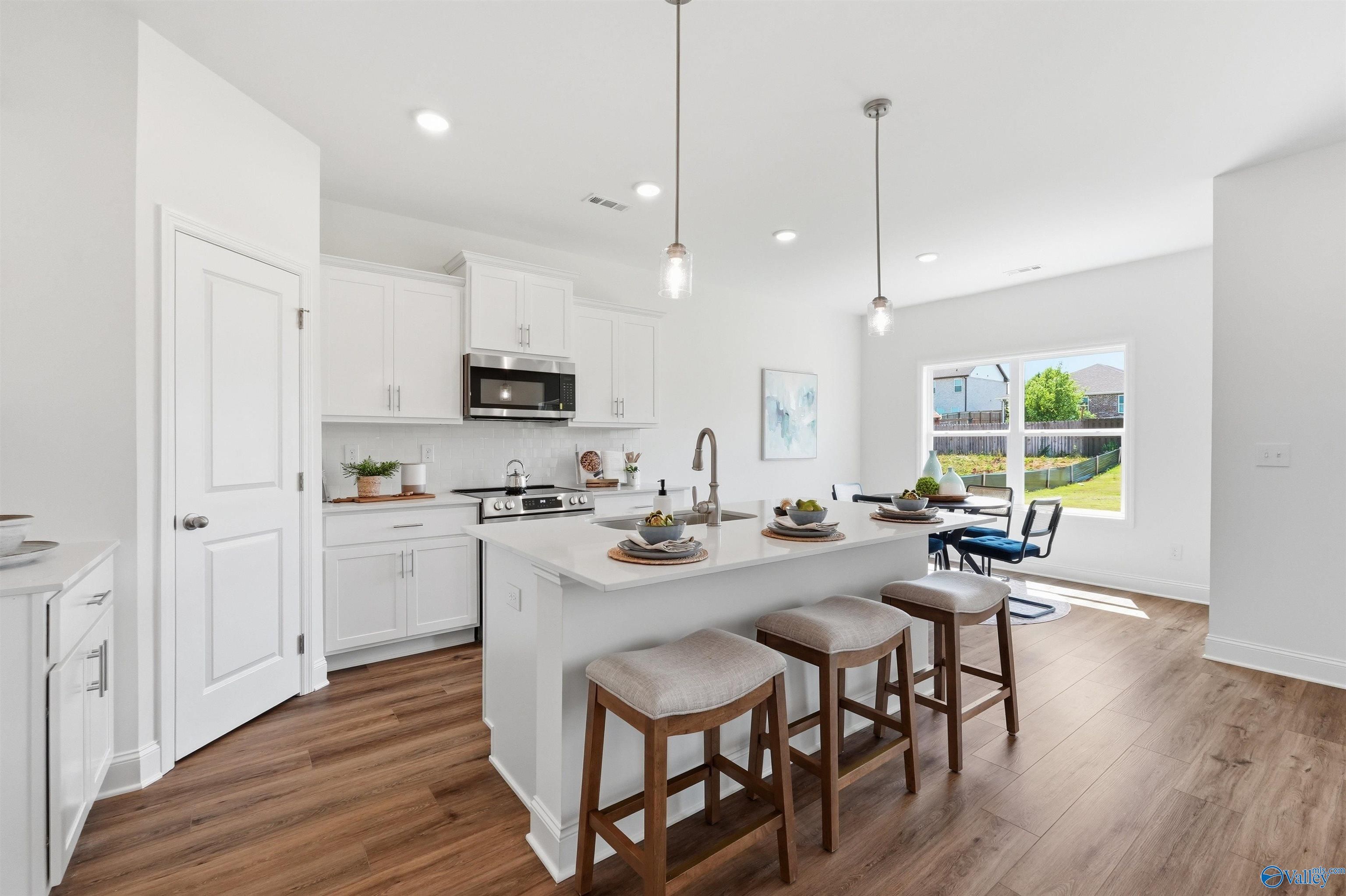 Modern kitchen with white cabinets, island seating, and stainless appliances in The Franklin C home, Meridianville, AL.