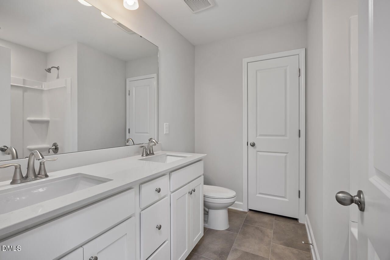 Modern bathroom with white dual vanity, tile floors, and shower in The Adalynn B floor plan at Gregory Village, Lillington.