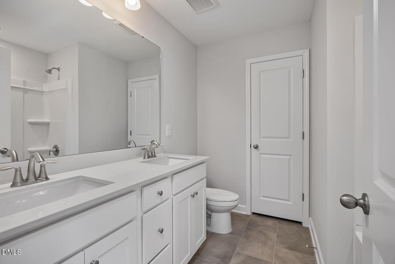 Modern bathroom with white dual vanity, tile floors, and shower in The Adalynn B floor plan at Gregory Village, Lillington.