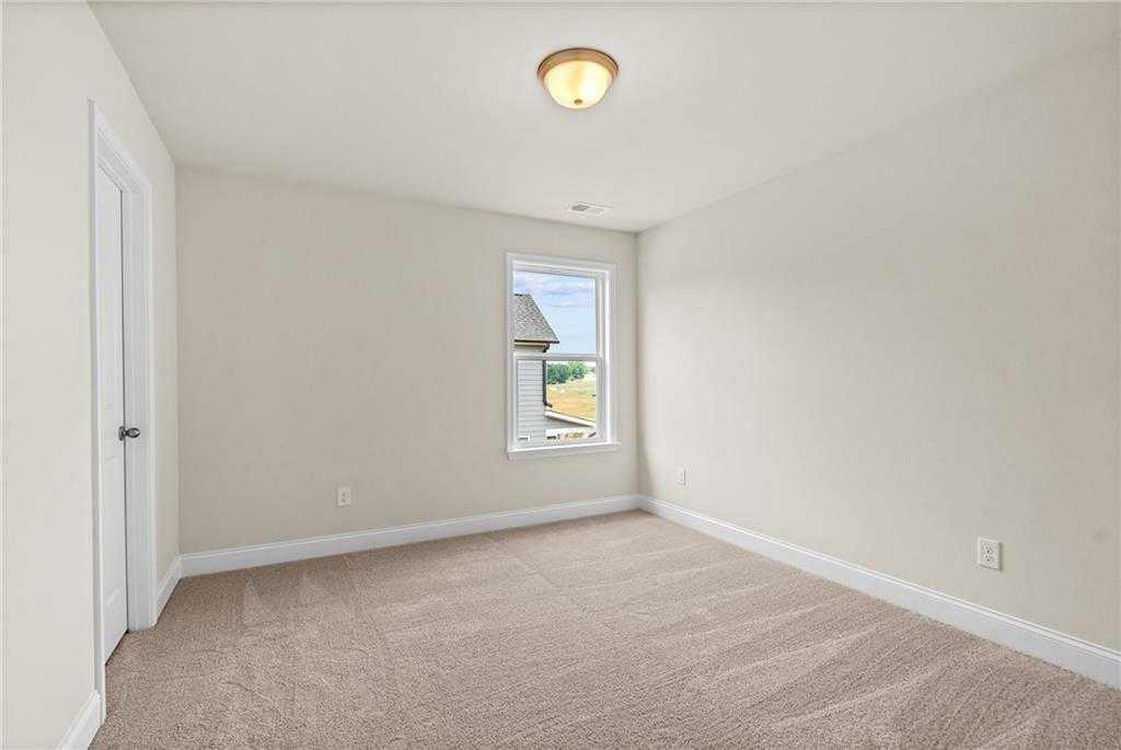 Bright secondary bedroom with beige walls, carpet flooring, and large window in Davidson Homes The Hickory B at Wehunt Meadows, Hoschton