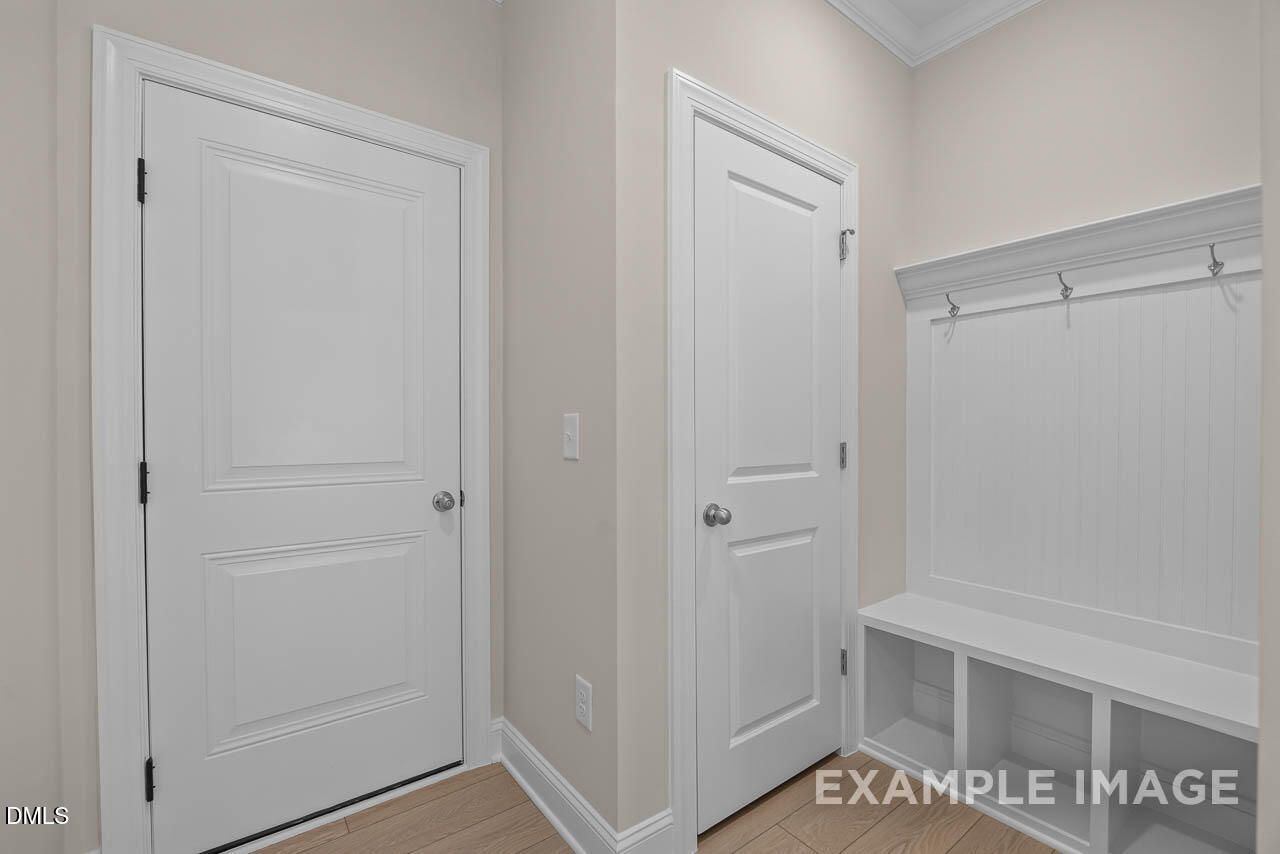 Functional mudroom with white doors, built-in bench, coat hooks, and storage shelves in Davidson Homes The Crawford D, Angier, NC