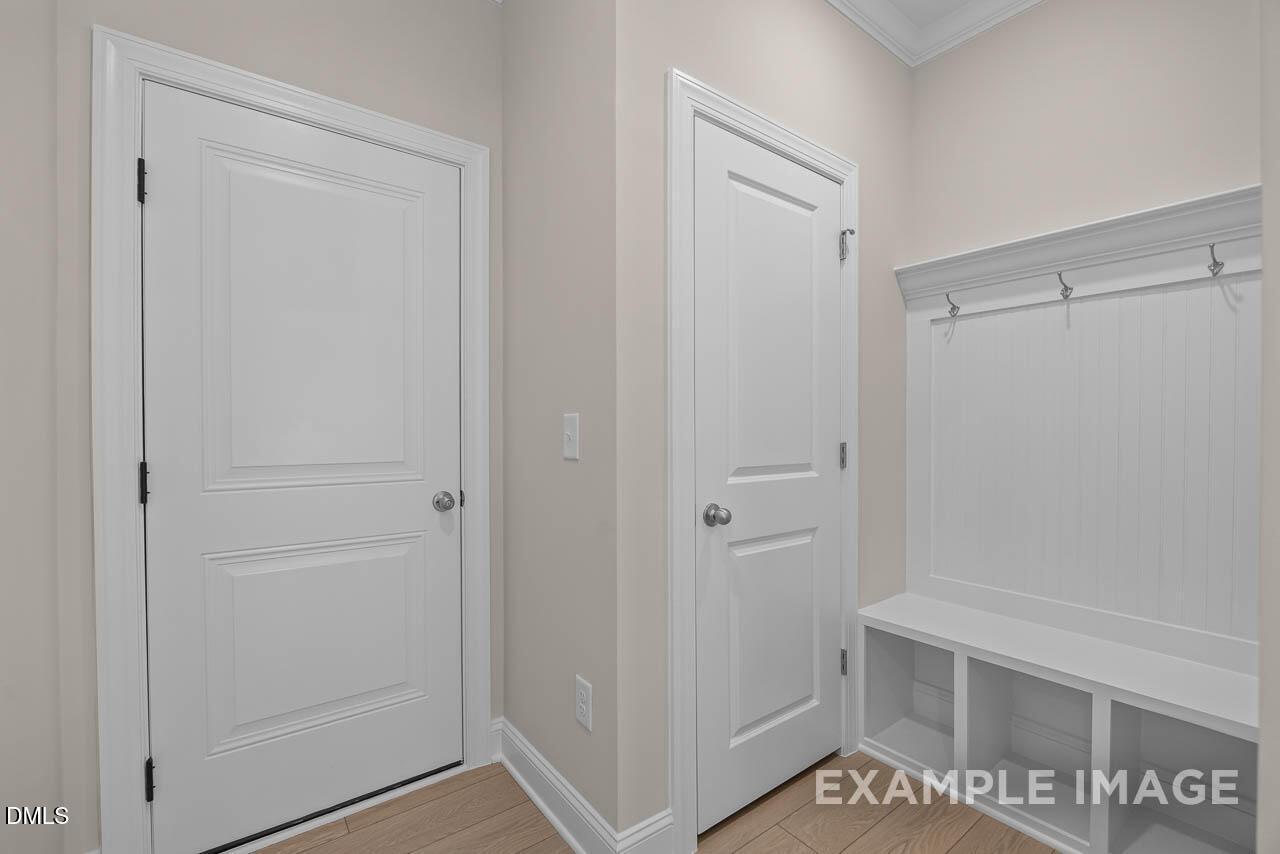 Functional mudroom with white doors, built-in bench, coat hooks, and storage shelves in Davidson Homes The Crawford D, Angier, NC