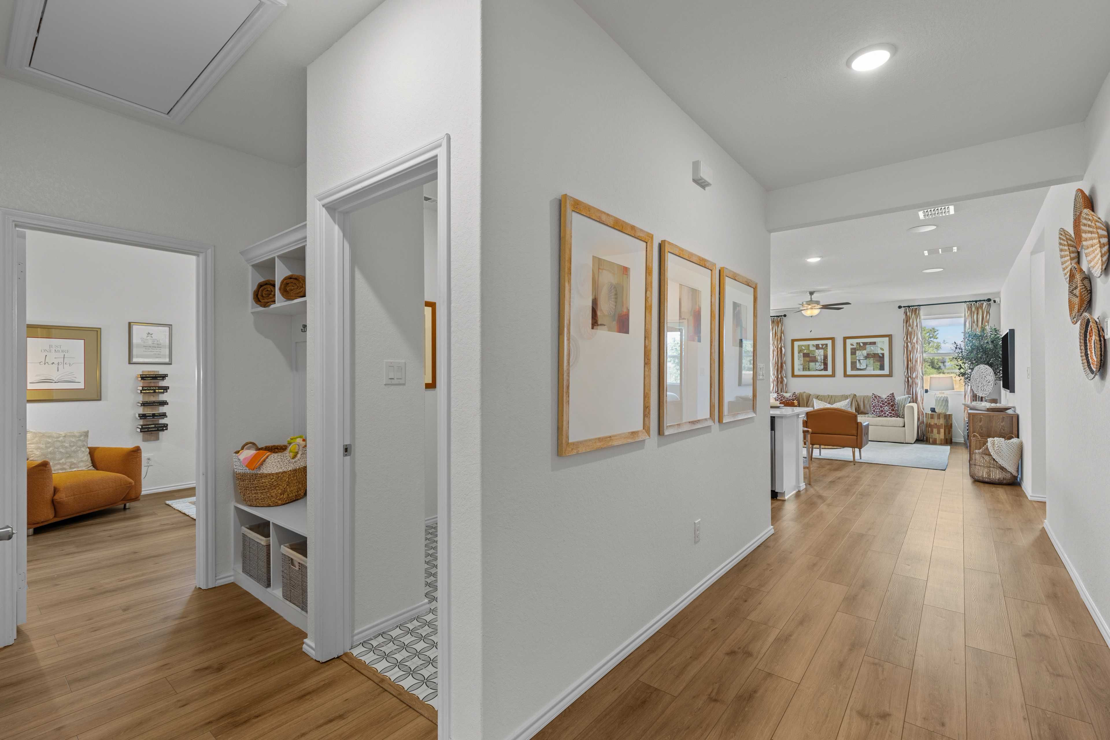 Spacious modern hallway in Rayburn Valley home, San Antonio TX with oak hardwood floors, white walls, framed art and open living area