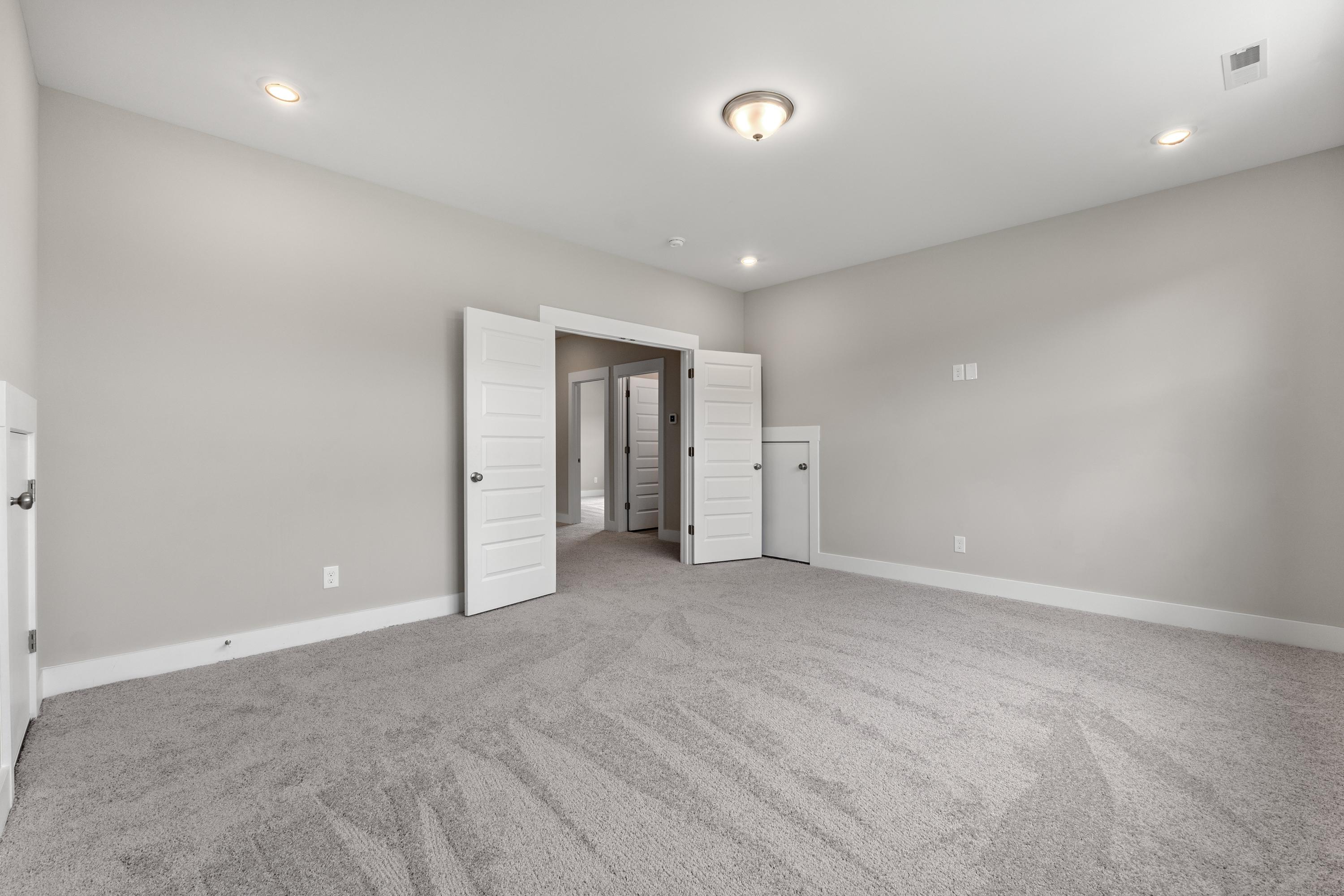 Spacious master bedroom in The Oxford C showcasing open double doors, light gray walls, plush carpet, and recessed lighting