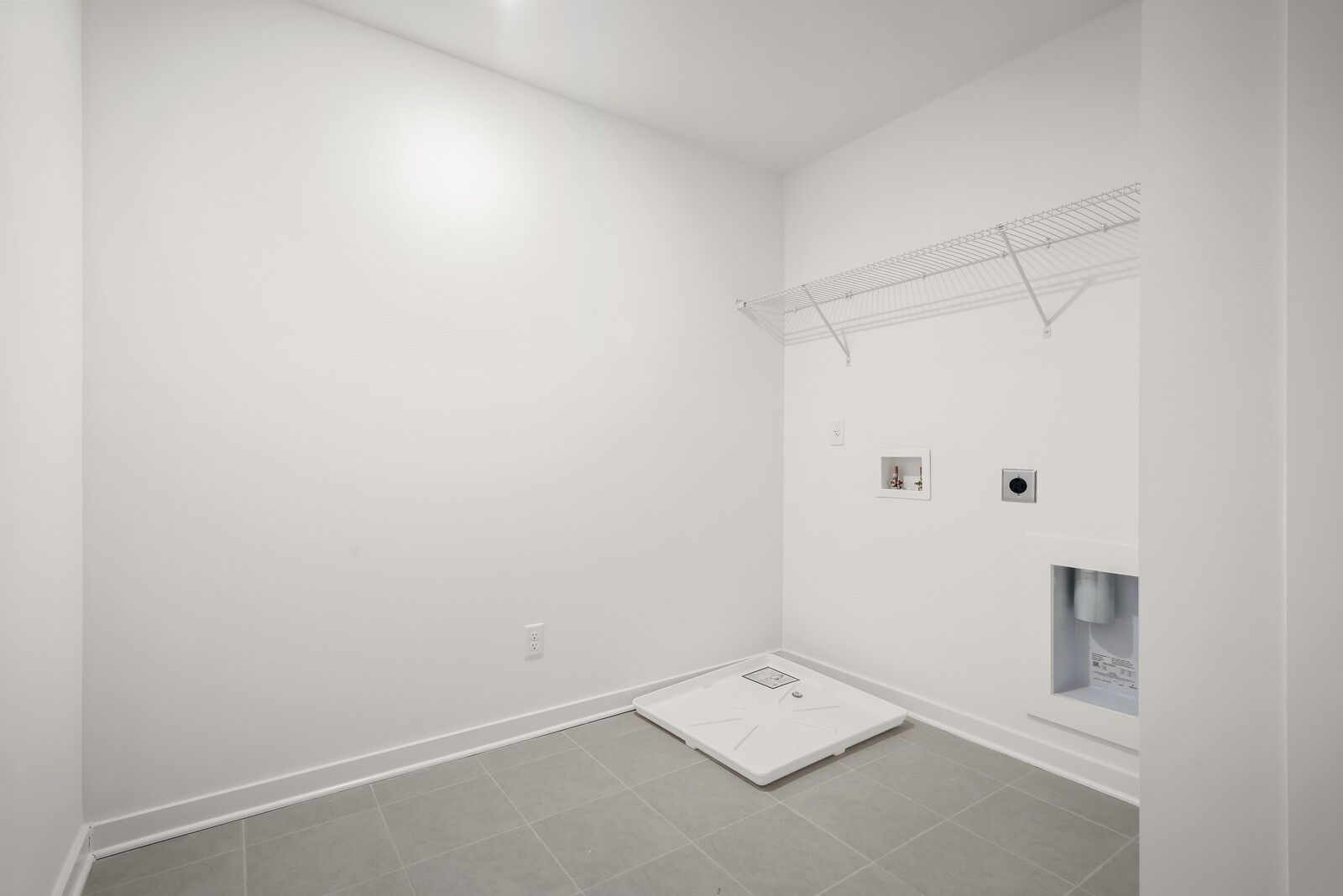 Spacious laundry room with open white shelving, washer dryer hookups, tiled floor in Davidson Homes The Logan C, Gallatin TN