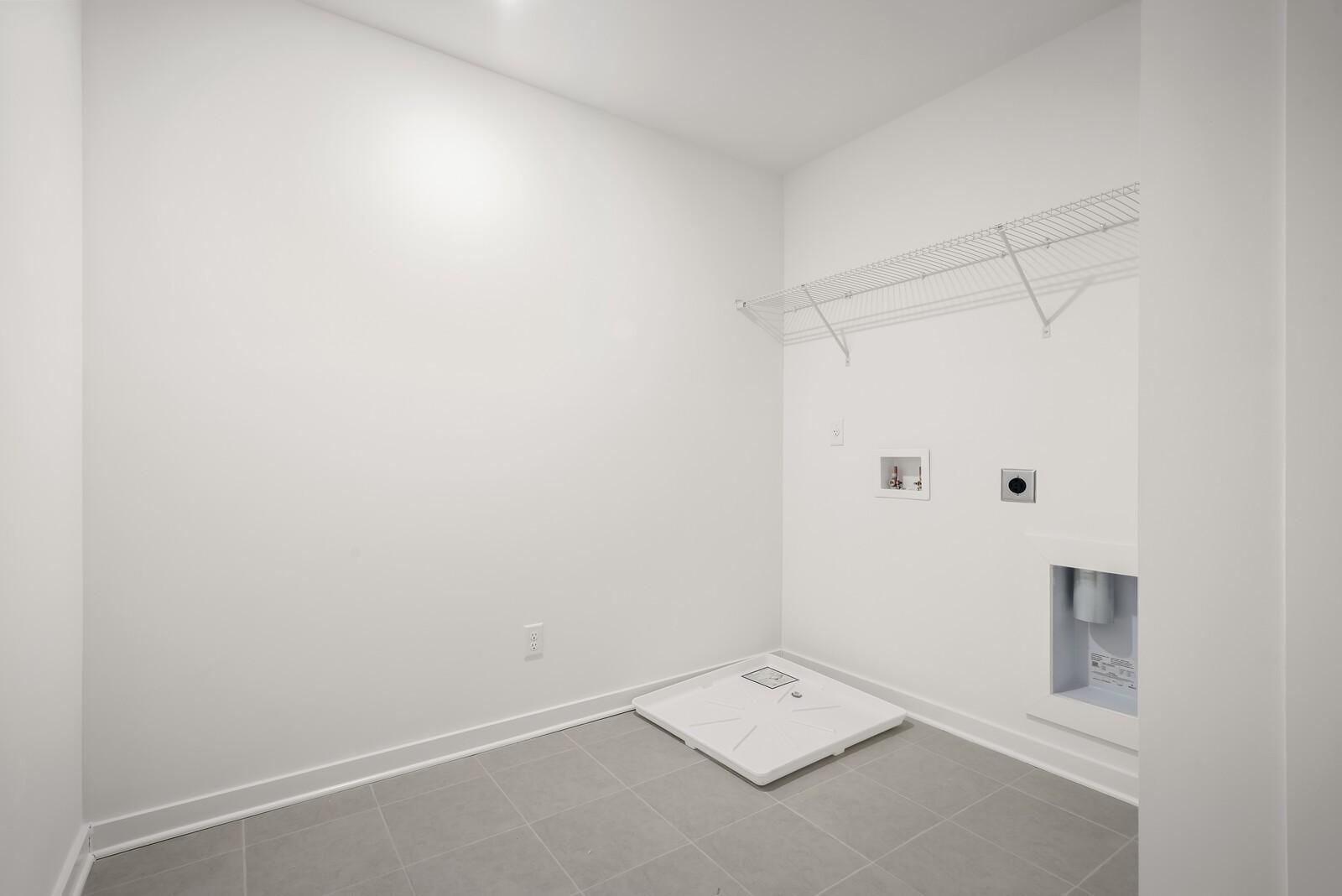 Spacious laundry room with open white shelving, washer dryer hookups, tiled floor in Davidson Homes The Logan C, Gallatin TN