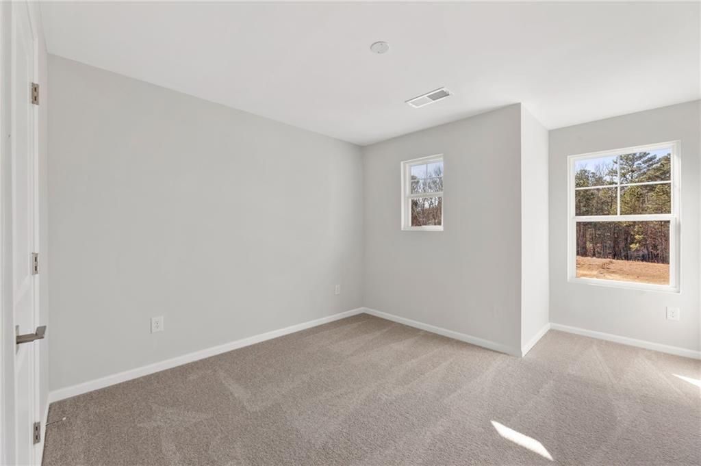 Bright secondary bedroom with light gray walls, beige carpet, and large windows overlooking wooded yard in Davidson Homes The Marion A, Winder, GA