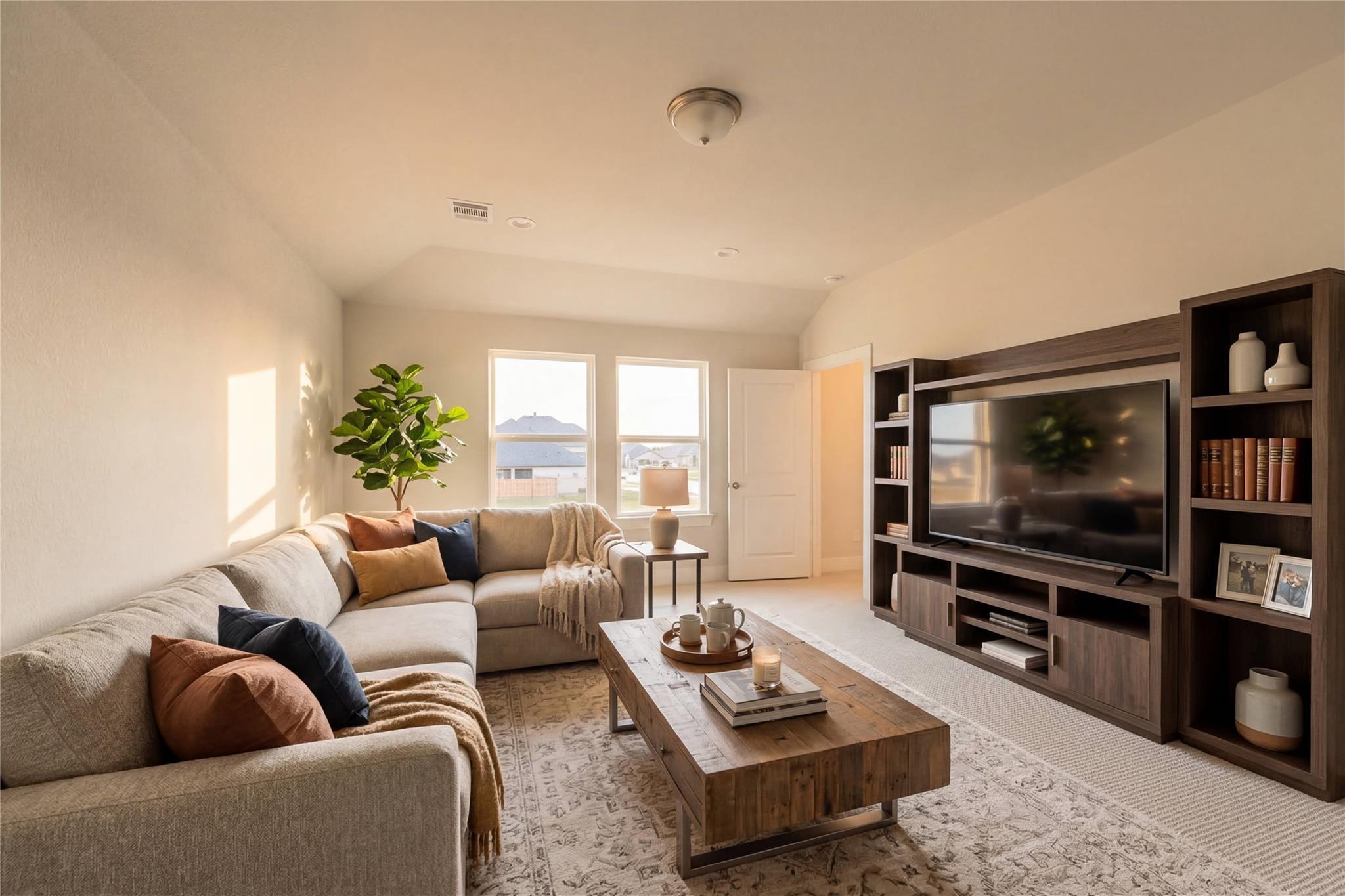 Cozy living room with gray L-shaped sofa, rustic wood coffee table, large wall TV, built-in shelves, and potted plants in Davidson Homes The Edward A, Lago Mar, Texas City