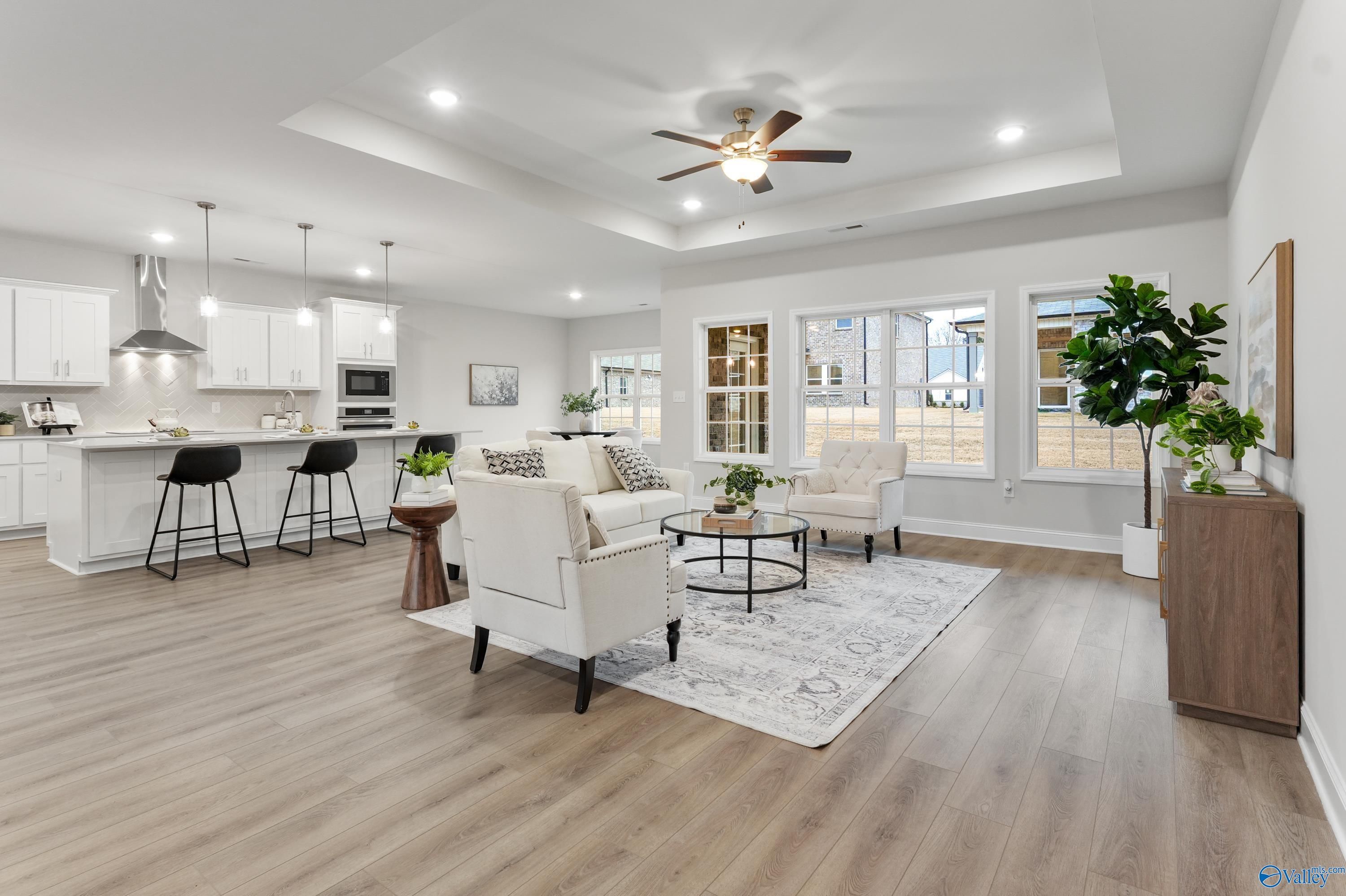 Open-concept living room with white sofas, coffee table, and adjacent kitchen island in Davidson Homes The Finleigh, Toney, Alabama