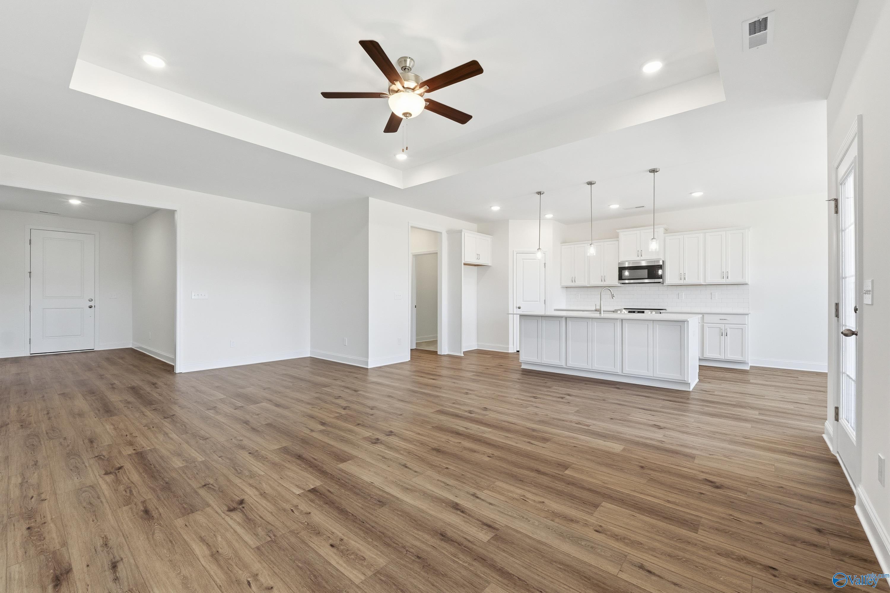 Open-concept kitchen with white cabinets, island, and hardwood floors in The Montgomery 3-bedroom home by Davidson Homes, Meridianville, AL