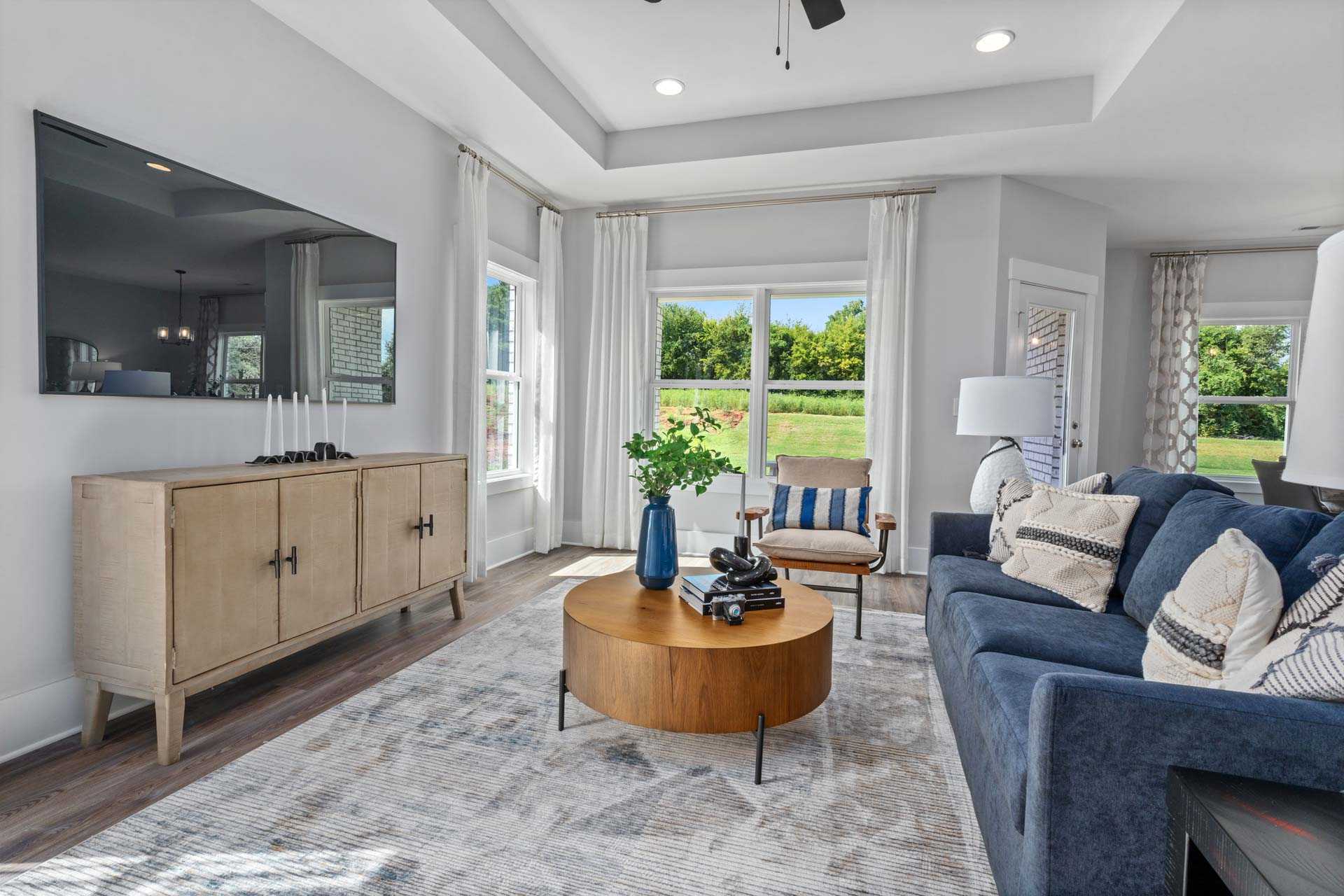 Spacious living room in Blue Spring Huntsville AL with navy sofa, wooden credenza, round coffee table, and large windows overlooking greenery