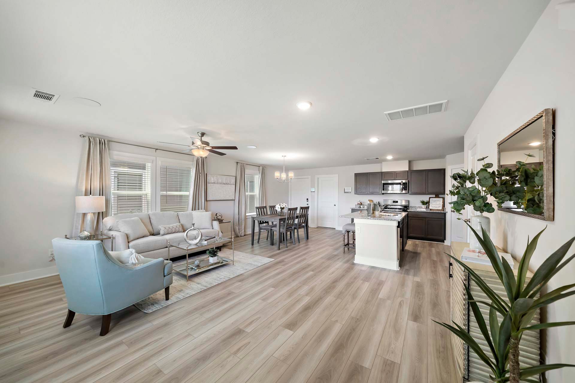 Open-concept living and kitchen at Enclave at Cypress in Cypress Texas featuring light wood floors, white island, and cozy seating