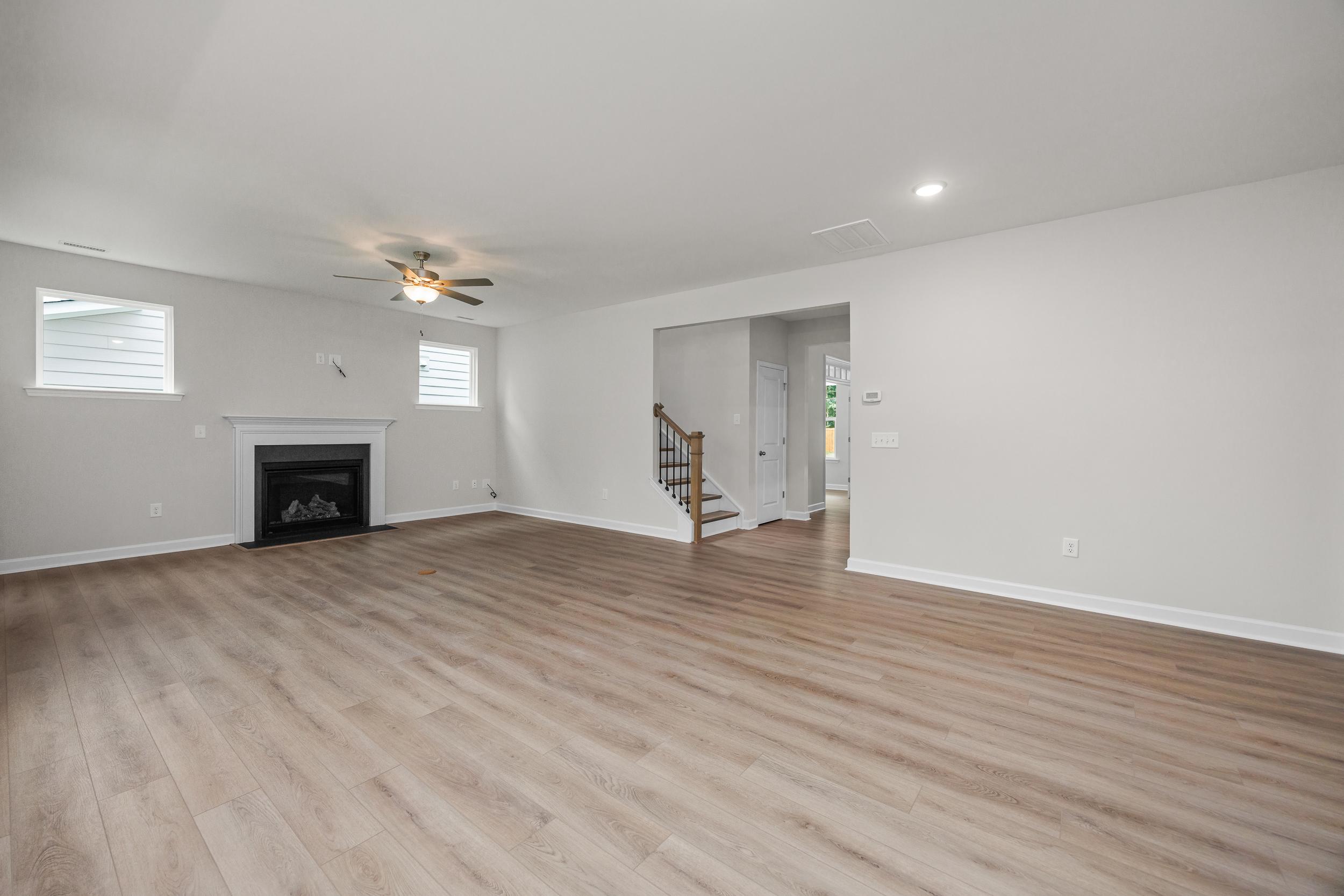 Spacious open-concept living room in The Aspen with hardwood floors, gas fireplace, ceiling fan, and staircase