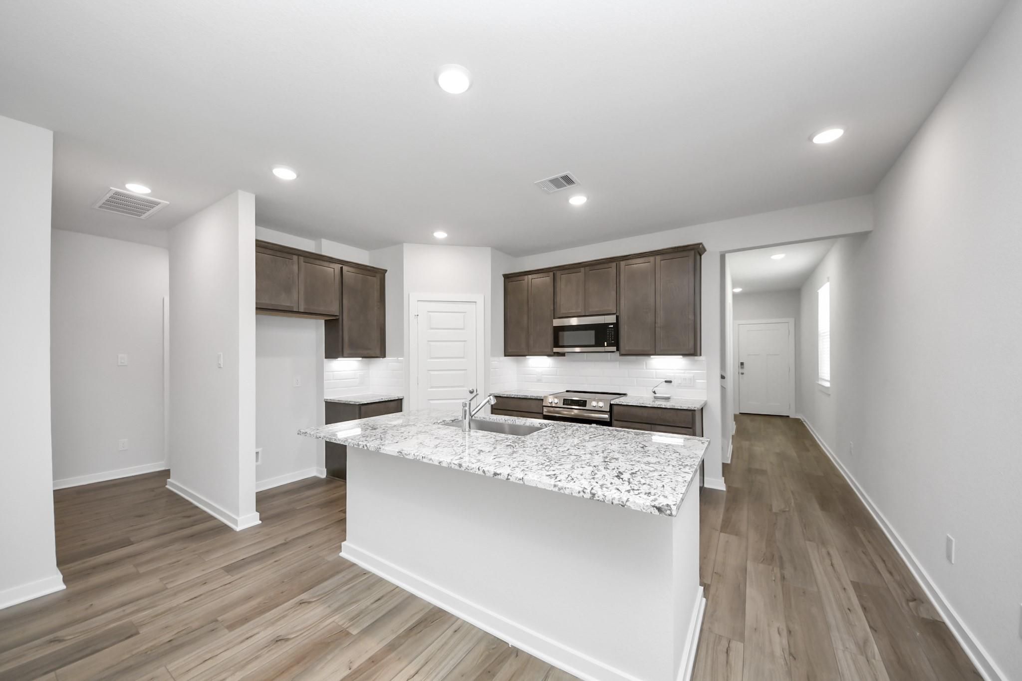 Modern kitchen with granite island and dark cabinets in The Sabine E floor plan at Liberty Estates, Cleveland, Texas.