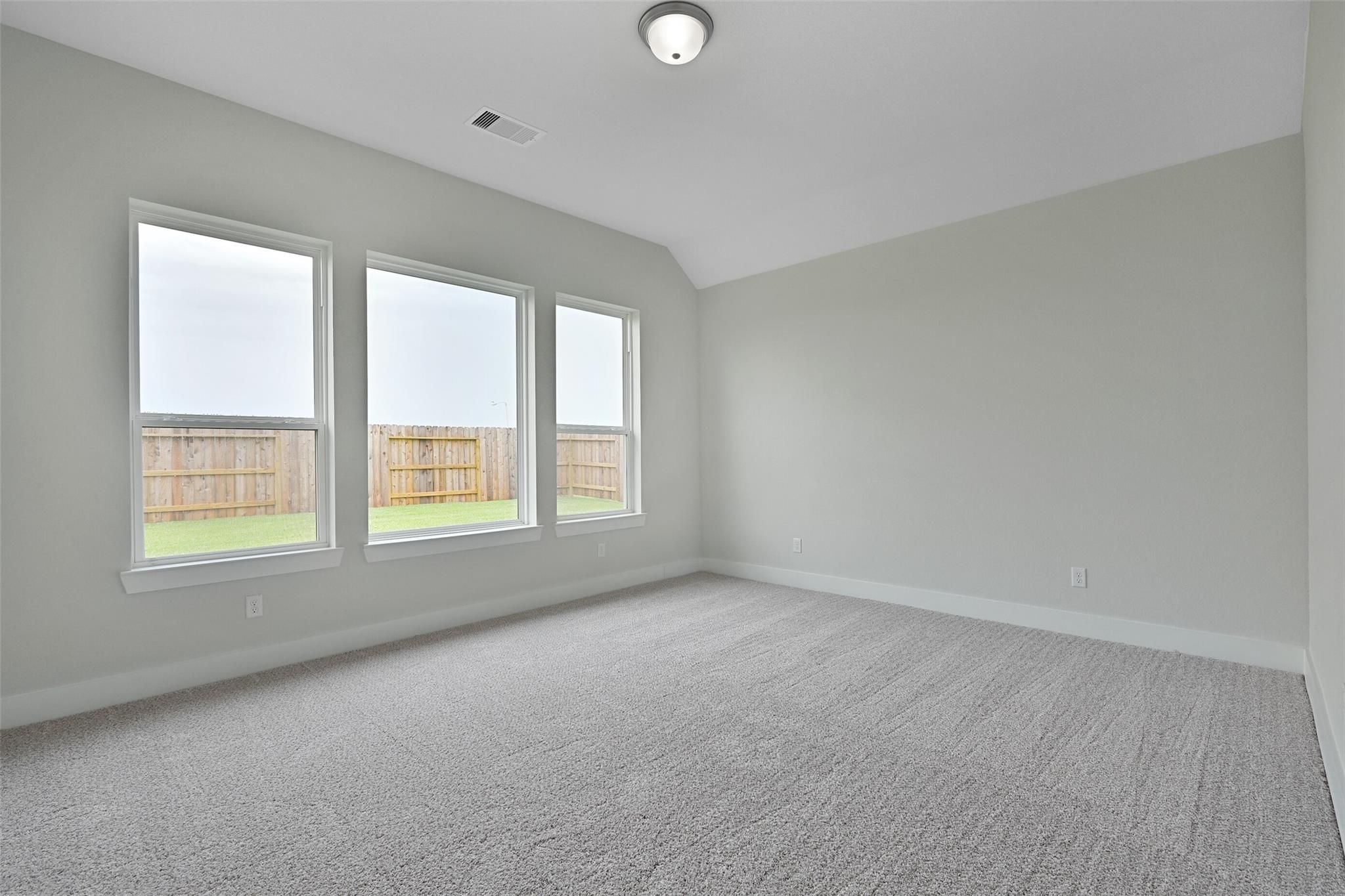 Spacious empty bedroom with gray walls, large triple windows to fenced backyard, carpeted floor in Davidson Homes The Edward C, Lago Mar, Texas City