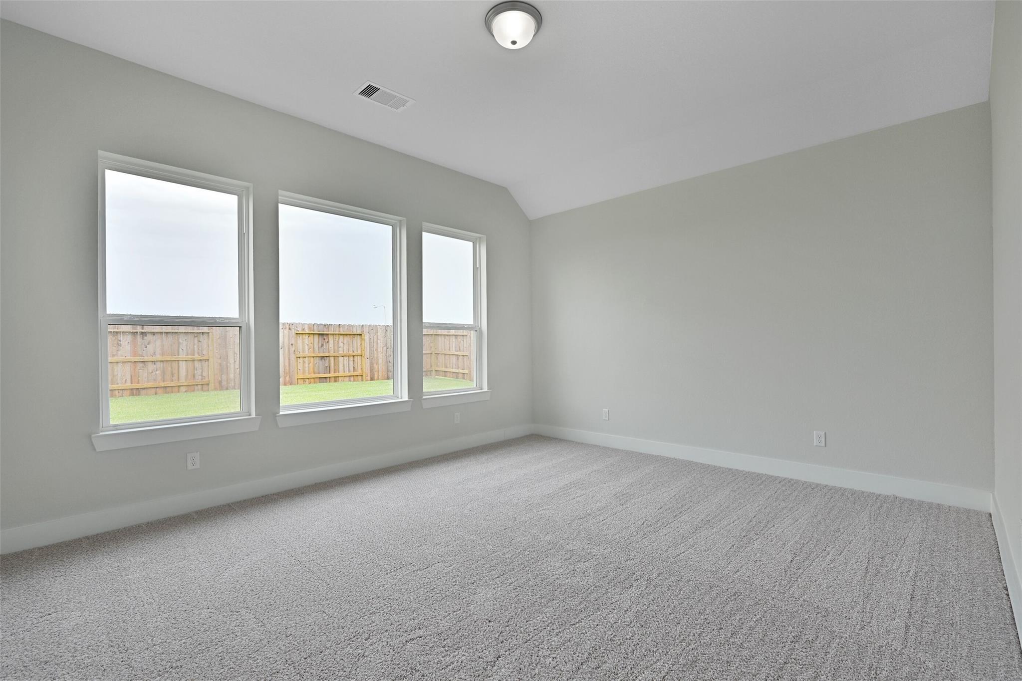 Spacious empty bedroom with gray walls, large triple windows to fenced backyard, carpeted floor in Davidson Homes The Edward C, Lago Mar, Texas City