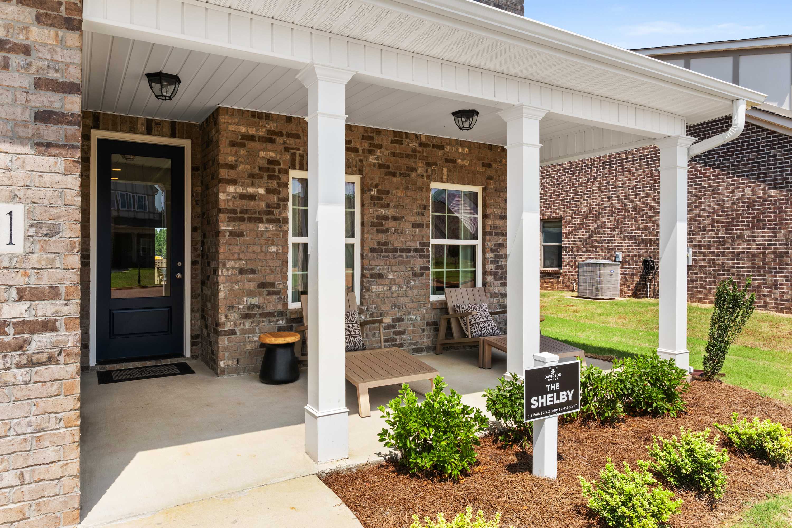 Charming brick Shelby model home exterior at Ricketts Farm in Athens, Alabama with covered front porch, blue door, and landscaped seating area