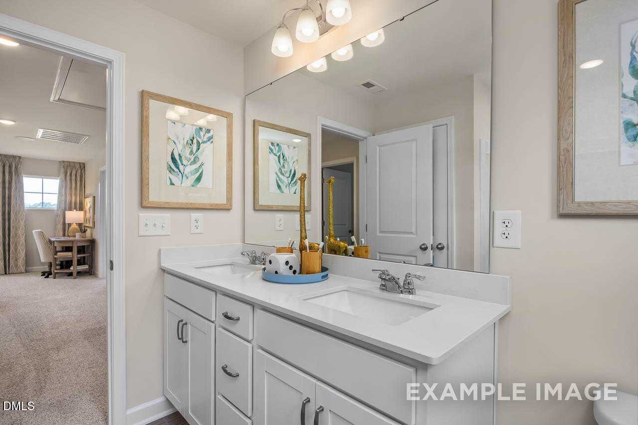 Modern double vanity bathroom with white cabinets, round mirrors, and leaf artwork in Davidson Homes The Willow B, Lillington, NC