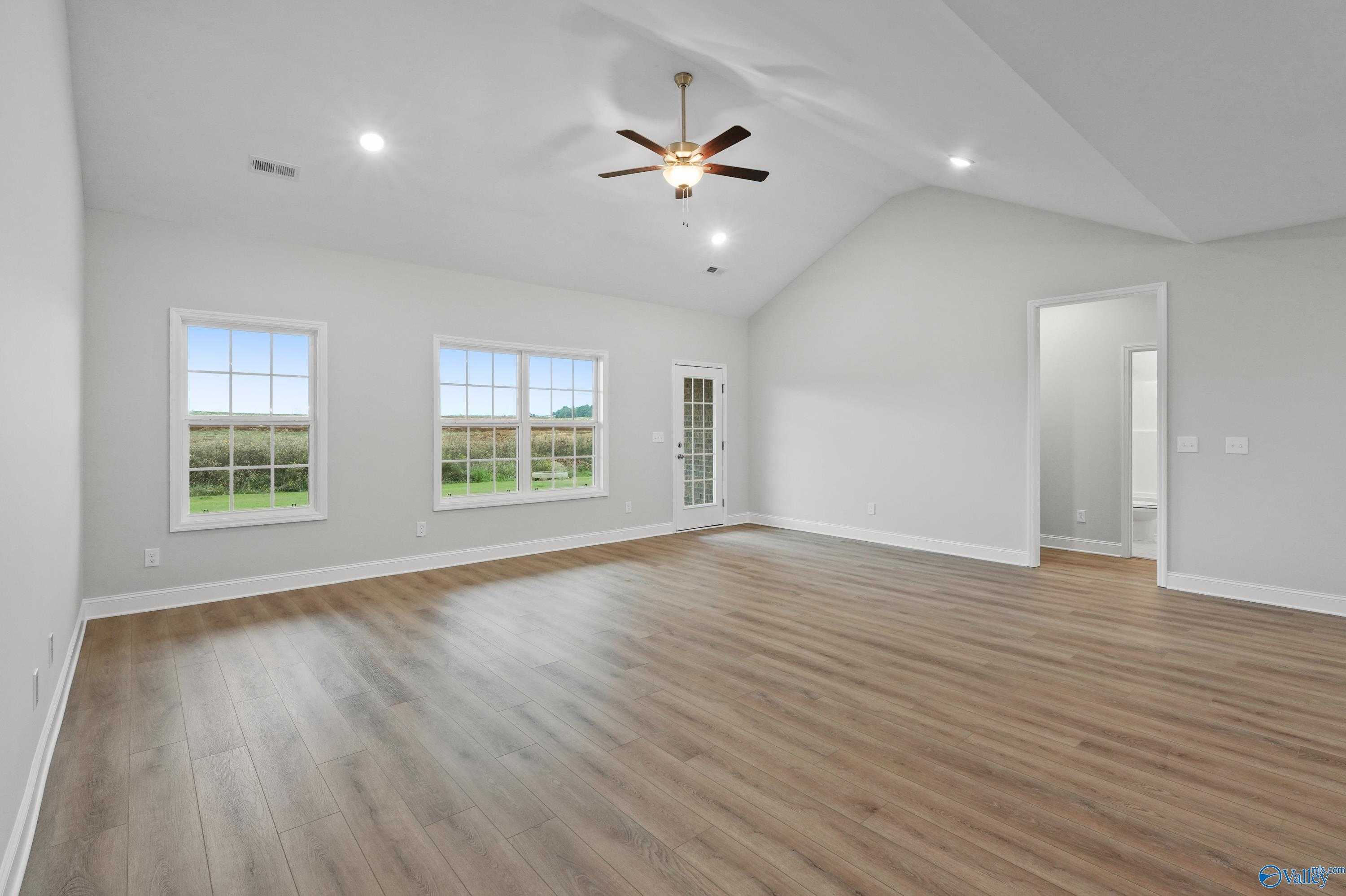 Spacious living room with hardwood floors, ceiling fan, and large windows to green fields in Davidson Homes The Lanier, Harvest, AL