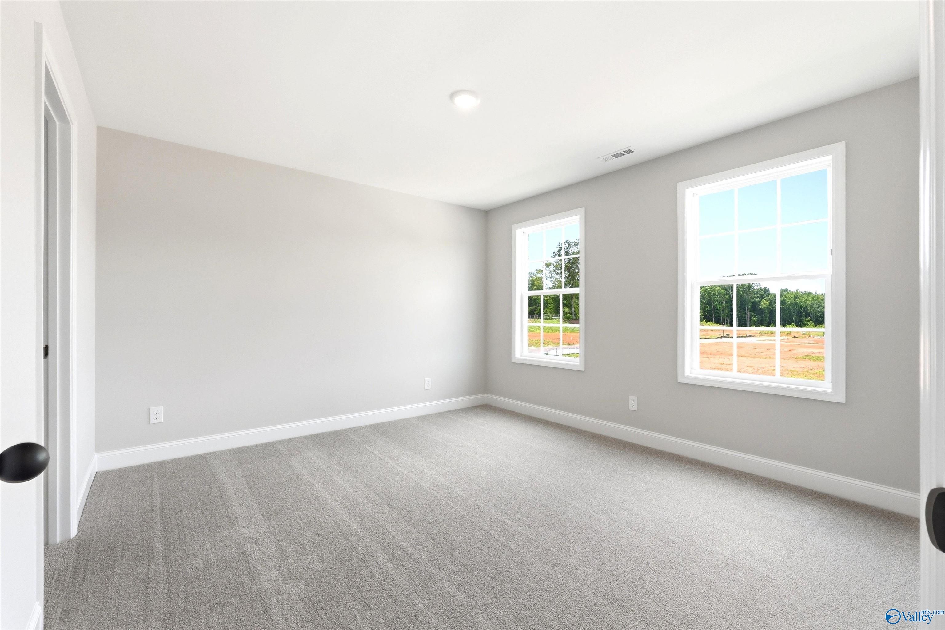 Bright, carpeted bedroom with neutral walls in The Shelby A floor plan at Wood Trail, Toney, Alabama.