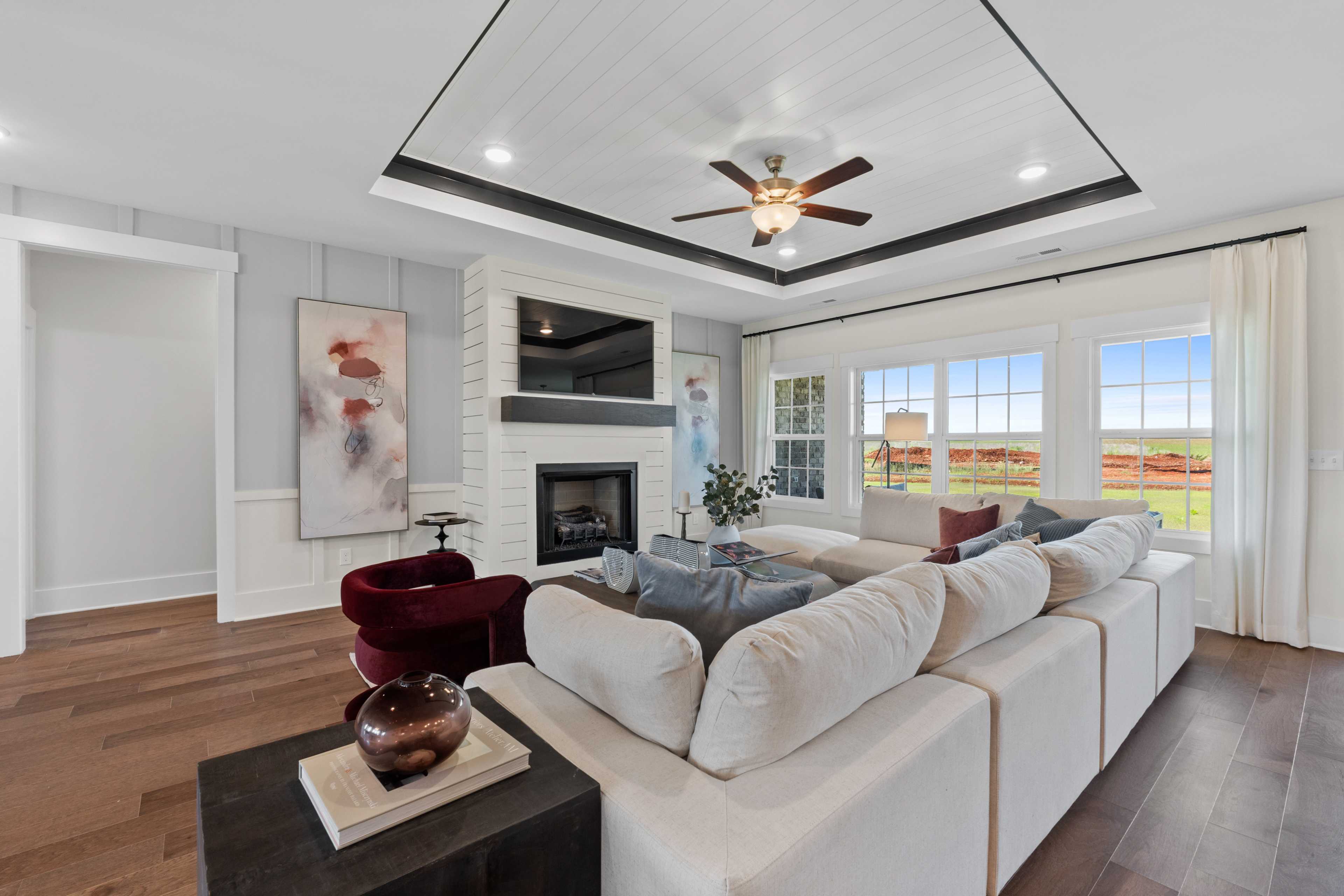 Spacious living room in Creekside, Harvest AL with white sectional sofa, fireplace, hardwood floors, large windows, and countryside view