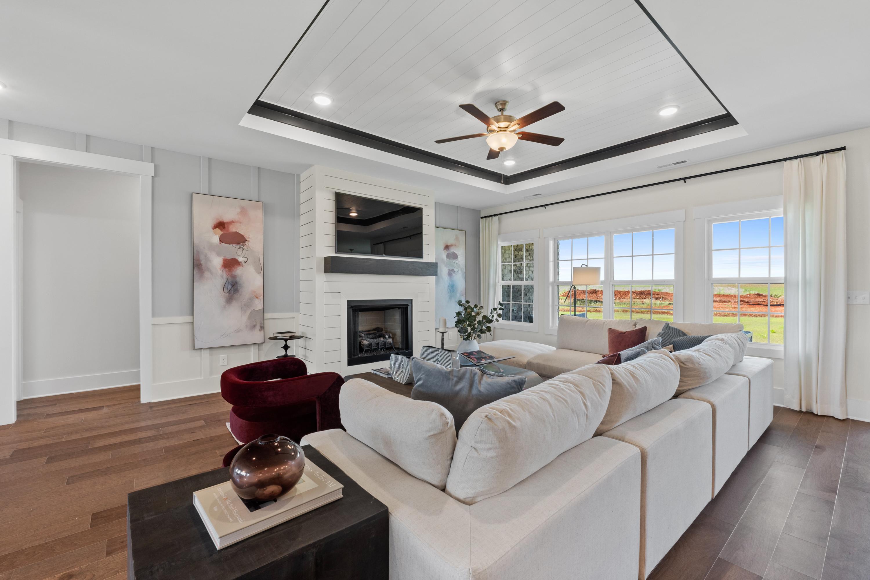 Spacious living room in Creekside, Harvest AL with white sectional sofa, fireplace, hardwood floors, large windows, and countryside view